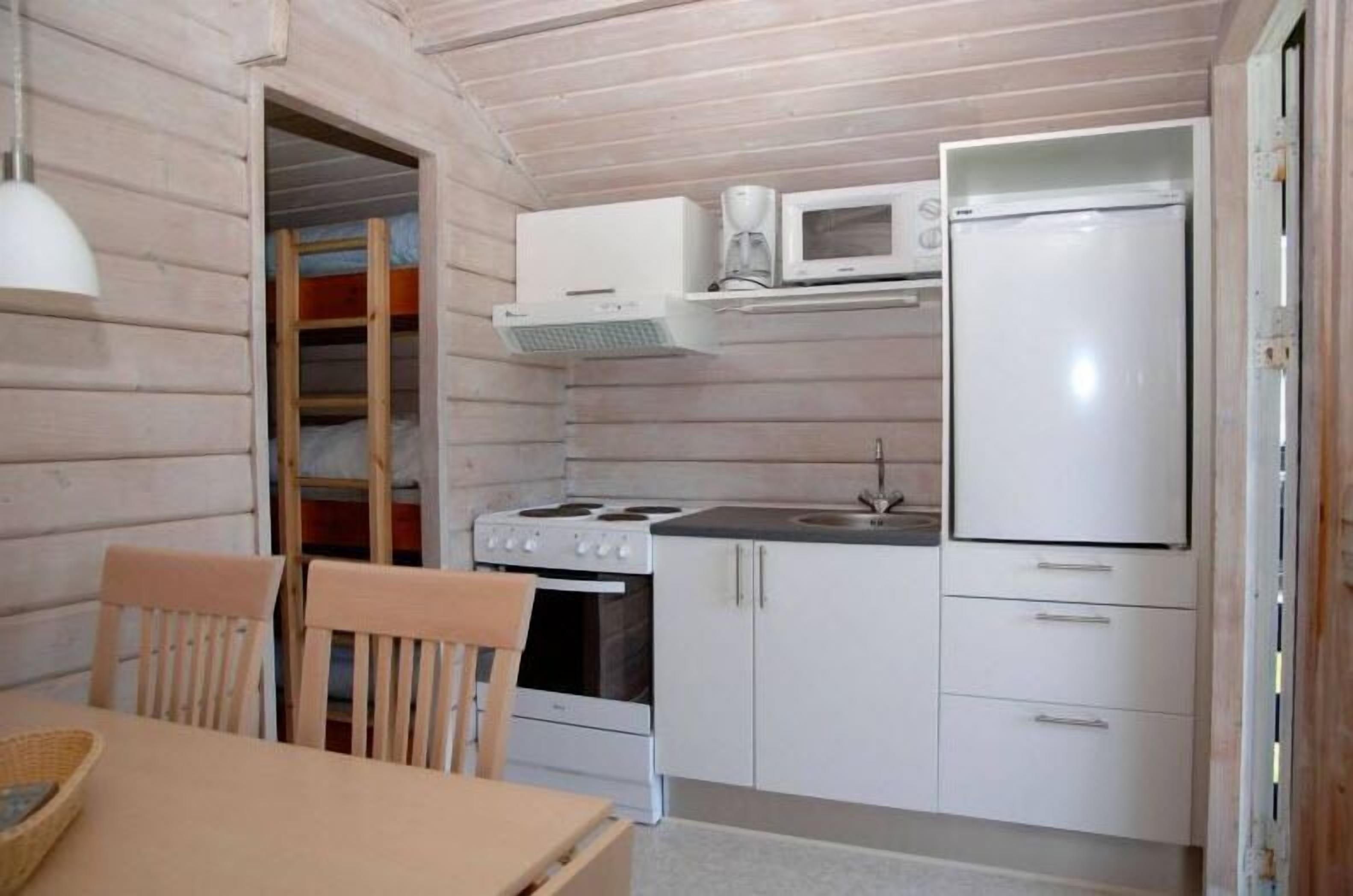 A compact kitchen with a stove, microwave, and refrigerator. There is a wooden dining table and chairs.