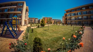 Un immeuble résidentiel doté de nombreux balcons, d’un terrain de jeux et d’une pelouse bien entretenue agrémentée de fleurs.