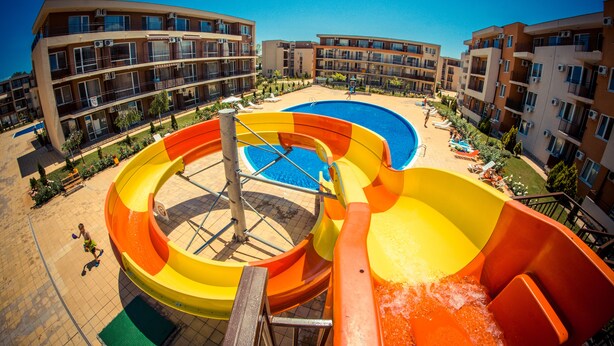 Un parc aquatique doté de nombreux toboggans et d’un espace piscine, entouré d’immeubles à plusieurs étages avec des balcons.