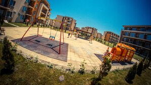 Un terrain de jeux avec des balançoires et un toboggan, entouré d’immeubles d’habitation.