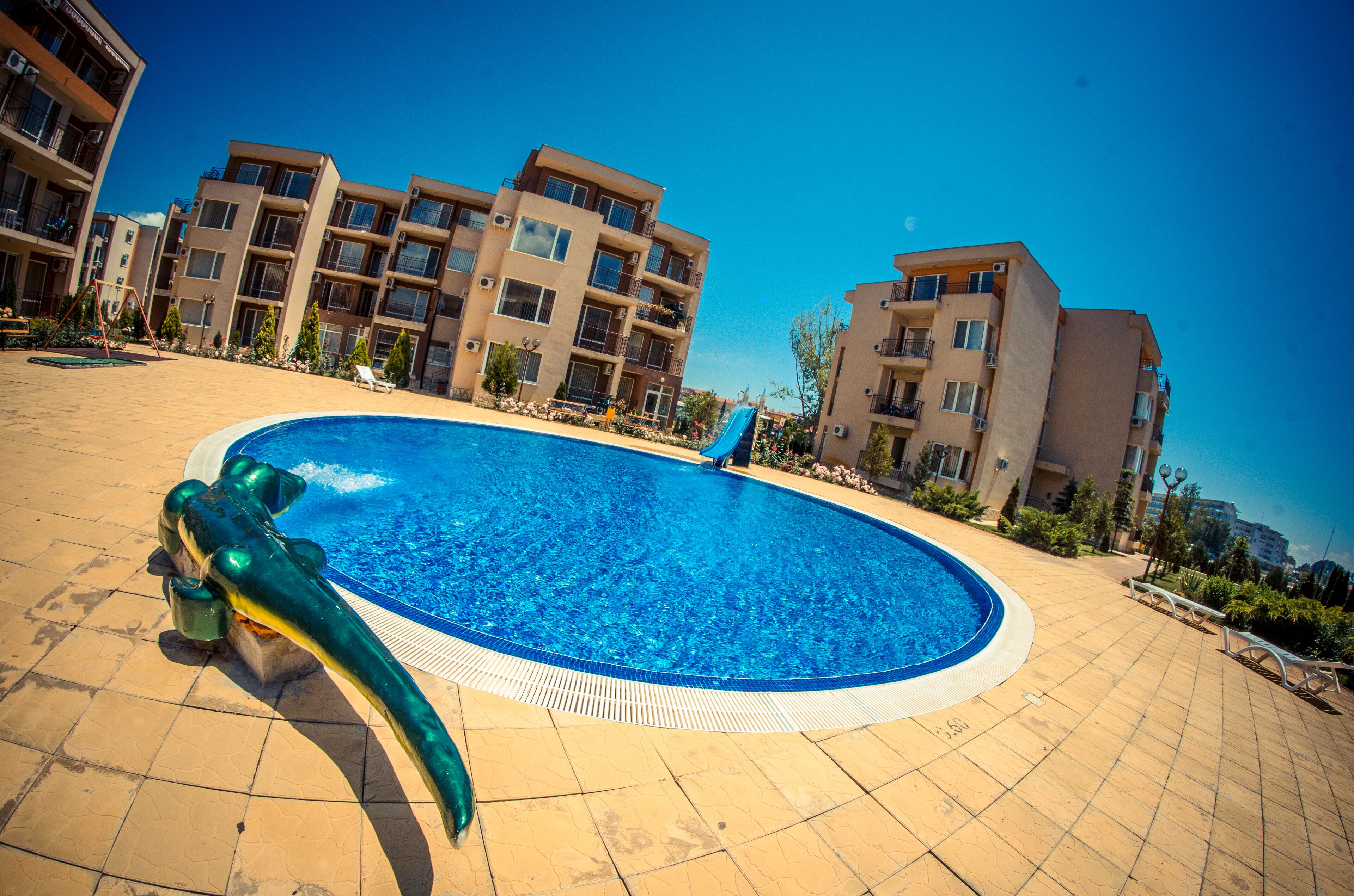 A swimming pool with a water slide, surrounded by multi-story buildings with balconies and air conditioning units.