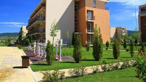 Un immeuble résidentiel à plusieurs étages, doté de balcons, d’une cour verdoyante et d’équipements de fitness en plein air.