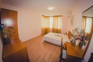 Ein Hotelzimmer mit Bett, Holzmöbeln, einem Spiegel und einem Fenster mit Vorhängen.