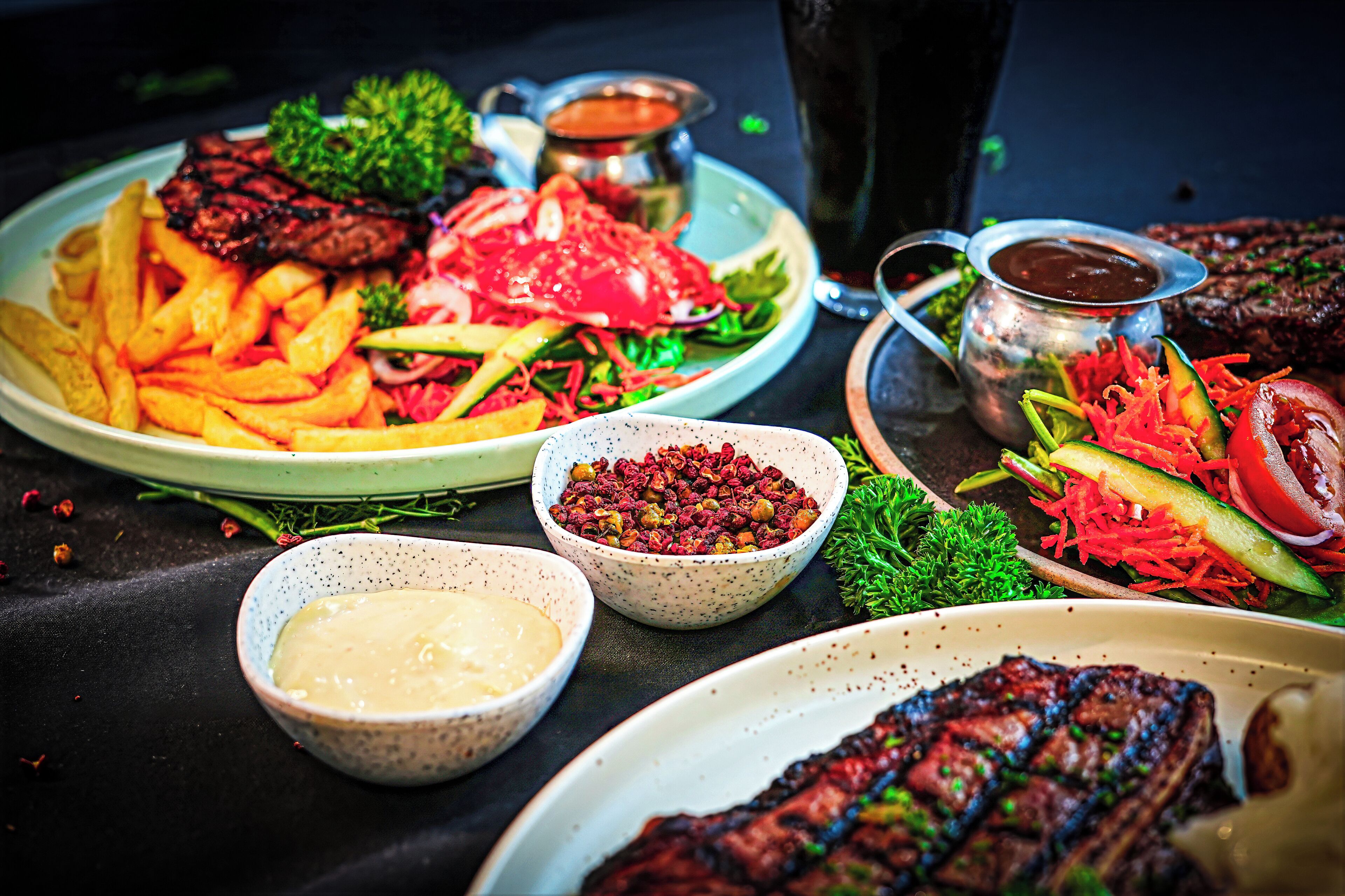Verschiedene Gerichte, darunter Steak, Pommes und Salate, serviert mit Beilagen.