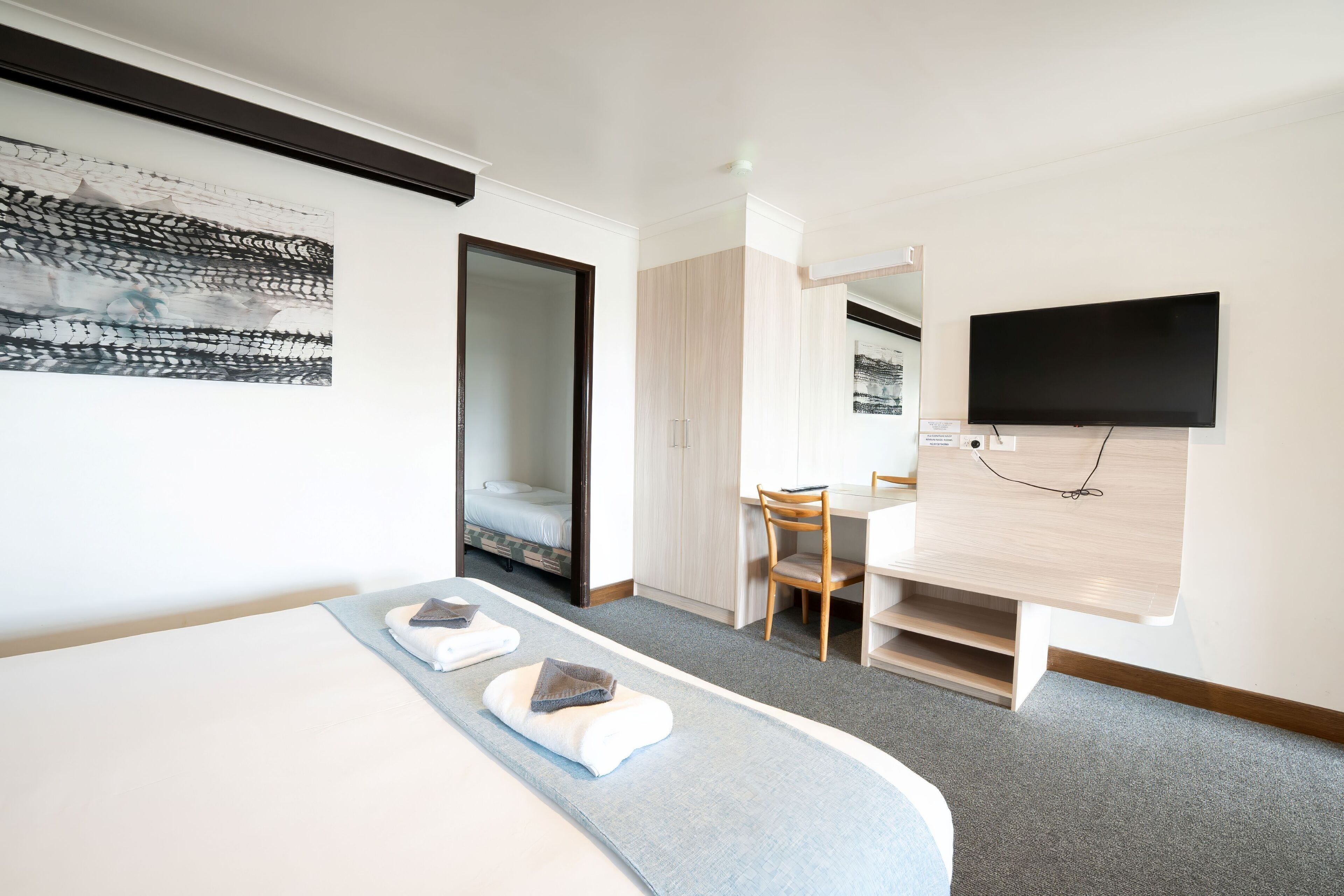 A hotel room with a bed, a desk, a chair, a television, and a door leading to another room.