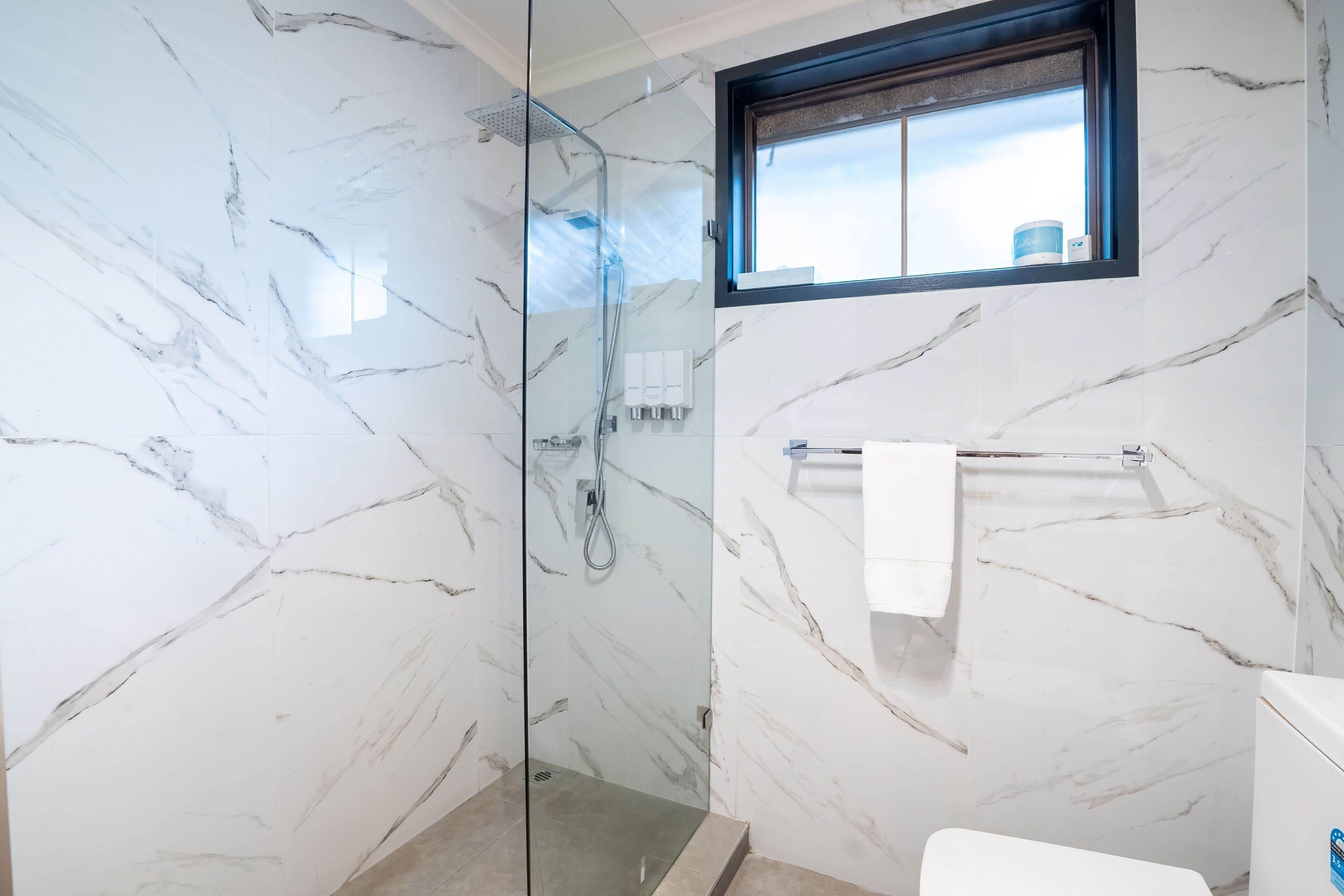 A bathroom with marble walls, a glass-enclosed shower, a window, and a towel rack.