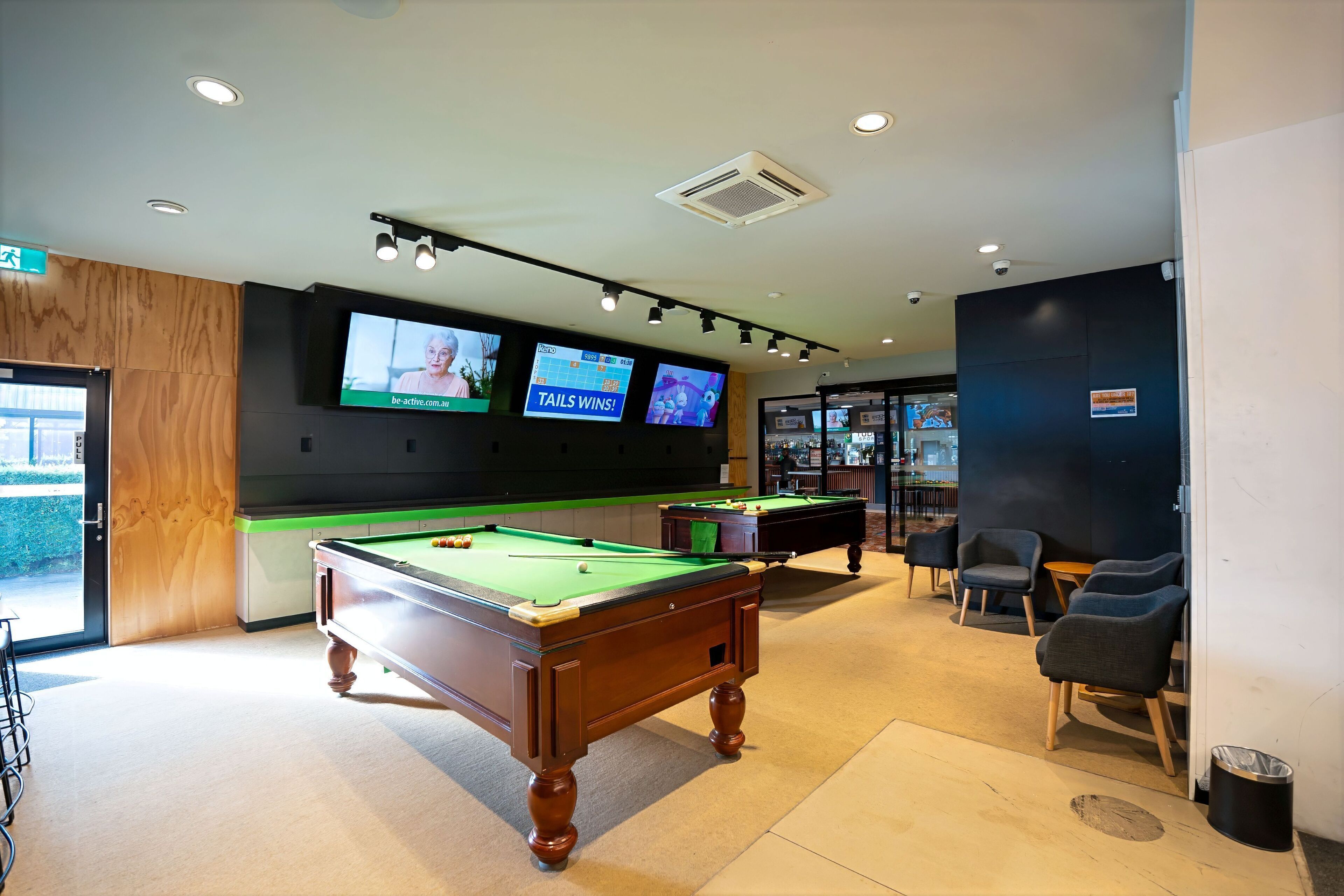 A pool table with two screens displaying sports content, a bar area, and seating.
