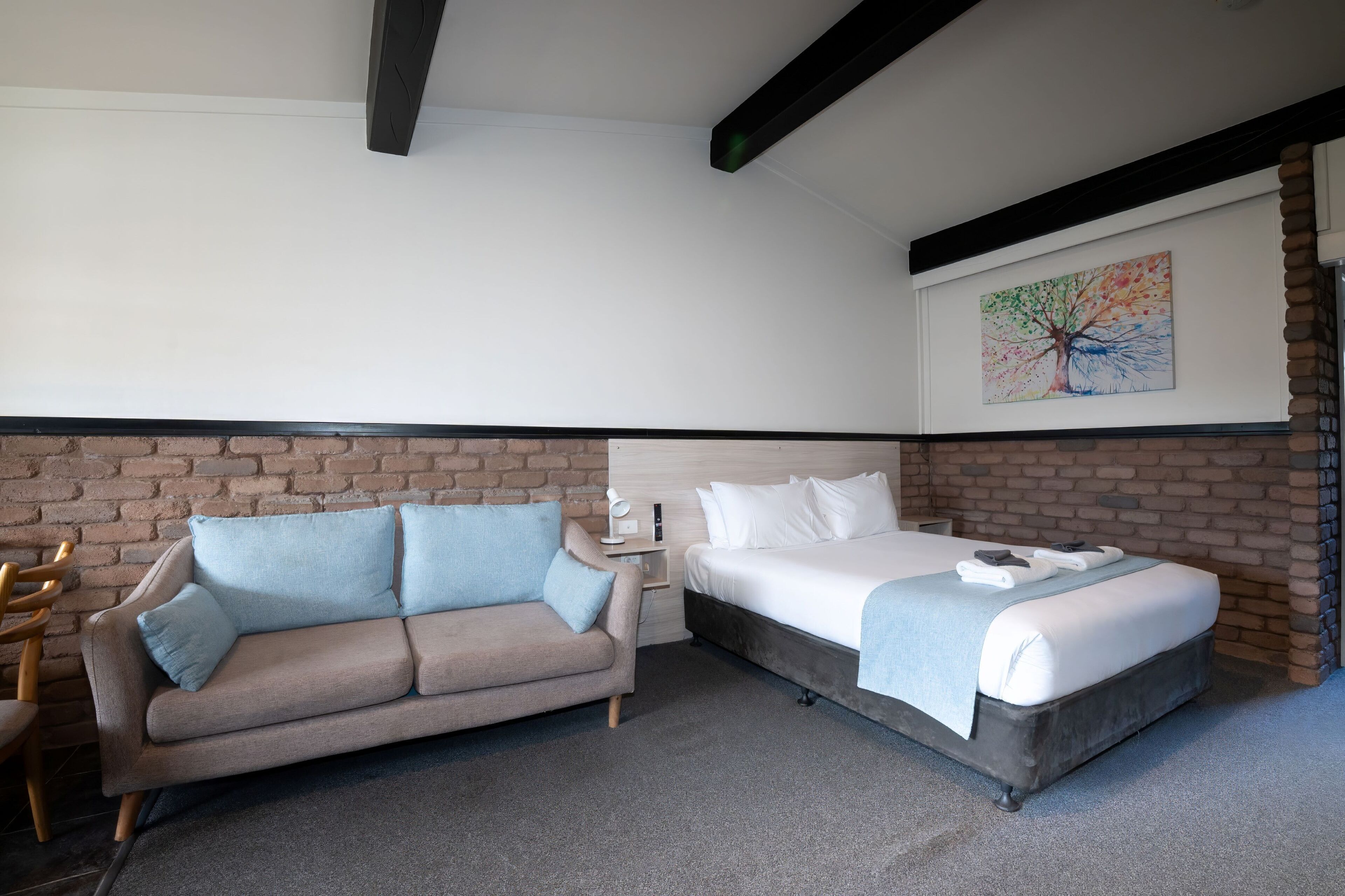 A hotel room with a bed, a sofa, a nightstand, and a wall-mounted painting.