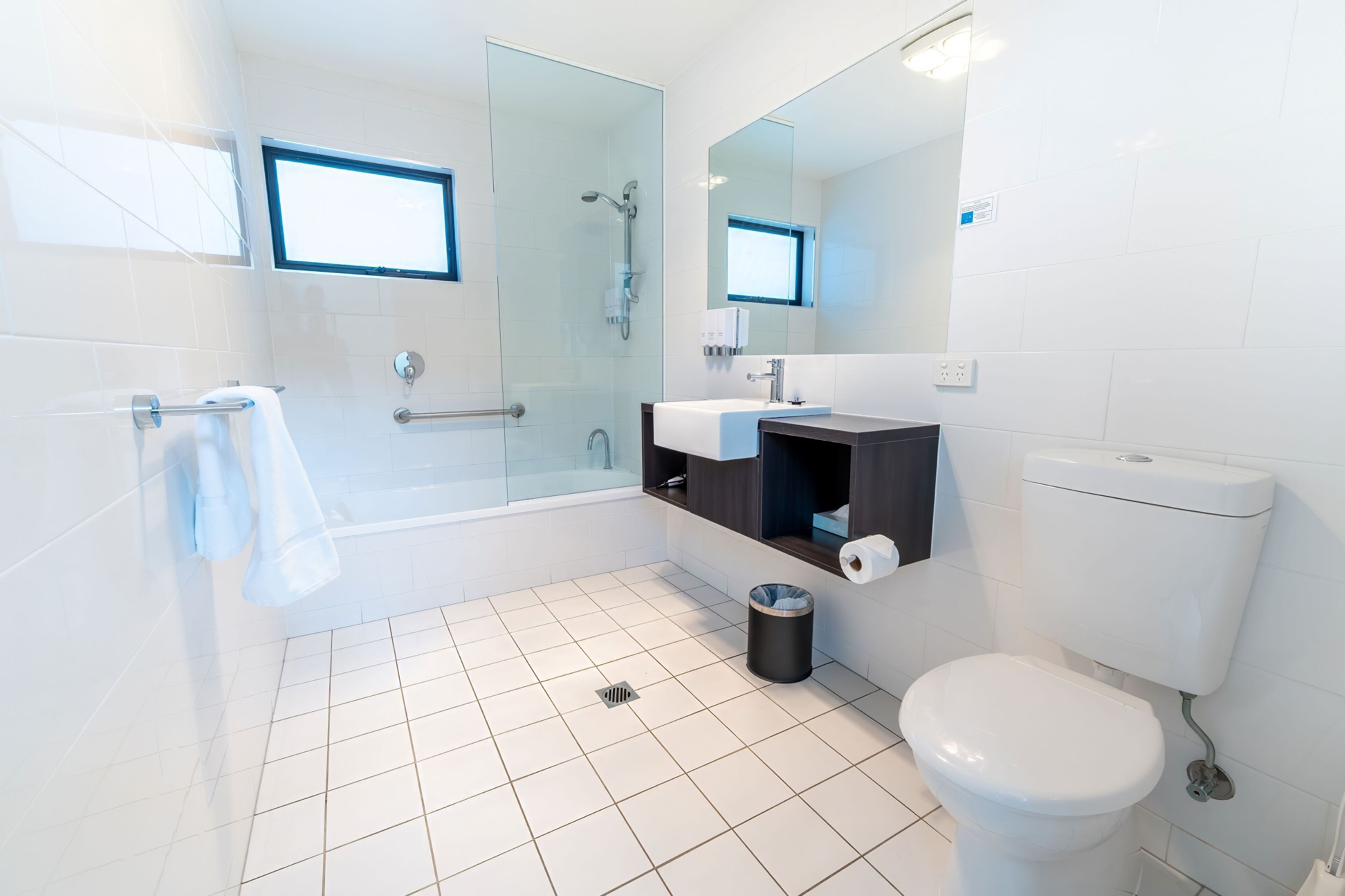 Une salle de bain moderne avec une douche à parois de verre, des toilettes blanches et un lavabo surmonté d’un miroir.