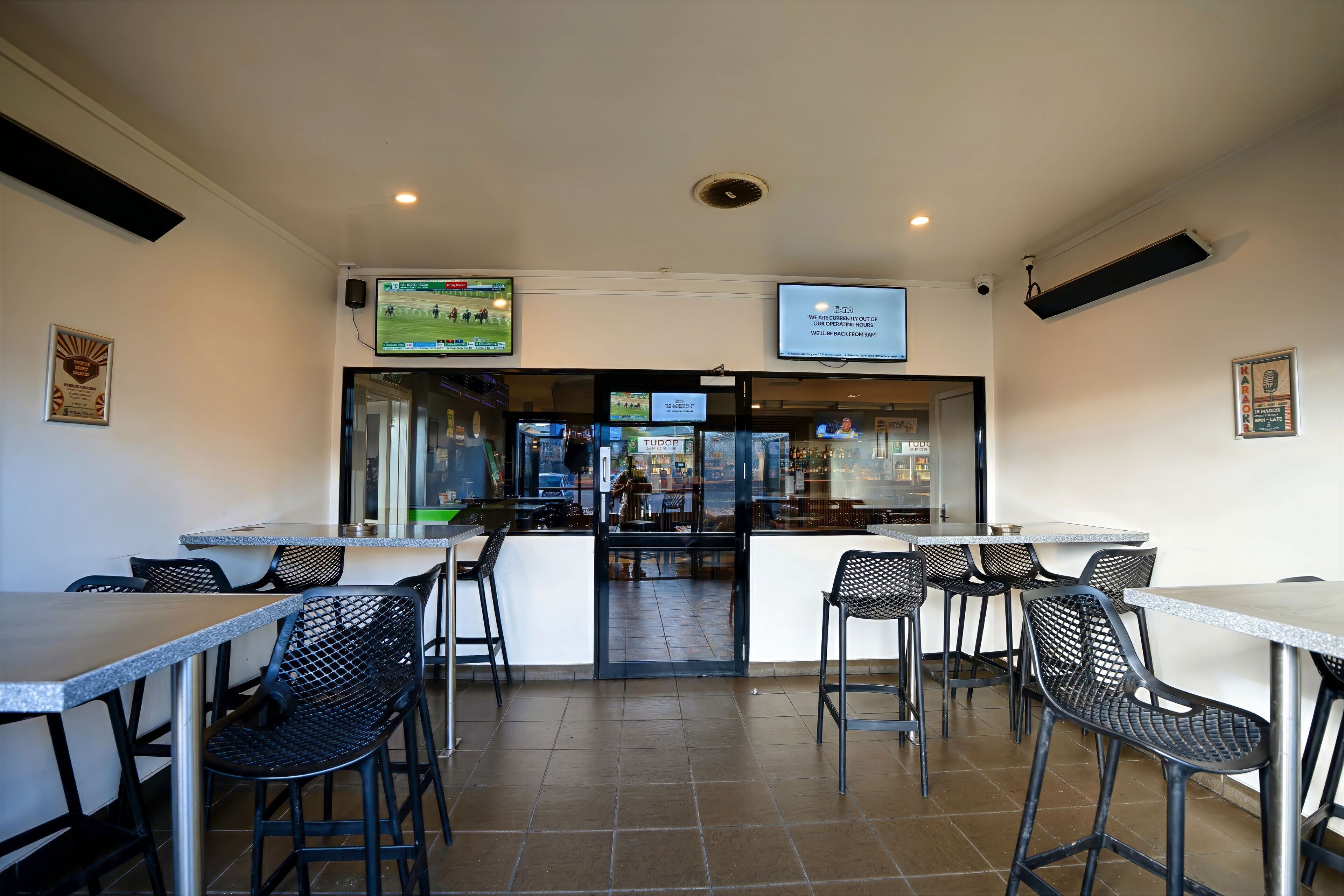 A restaurant with multiple tables and chairs, a counter, and a television screen displaying a sports event.