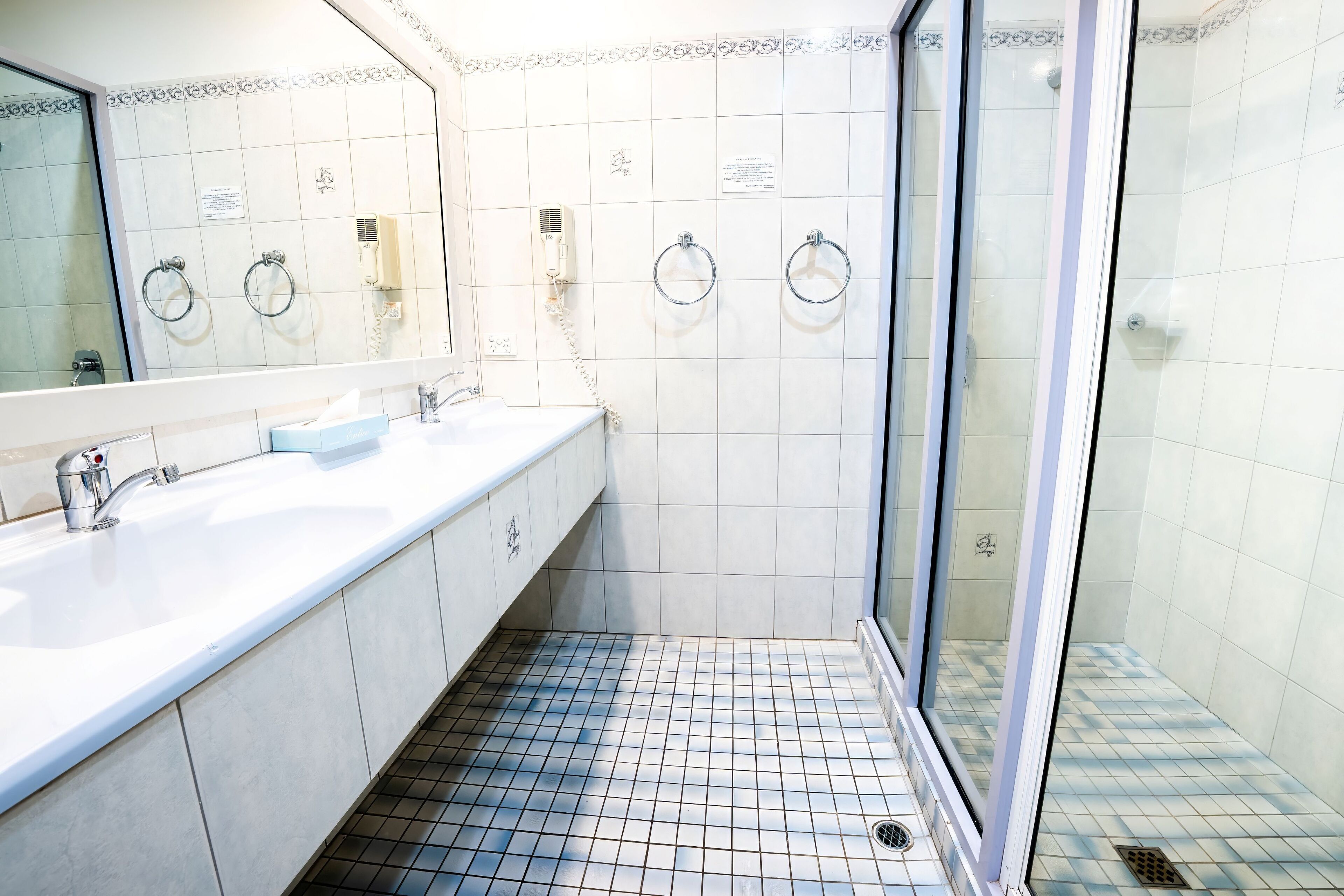 Une salle de bain dotée d’un grand miroir, de deux lavabos, d’une douche en verre et de murs carrelés.