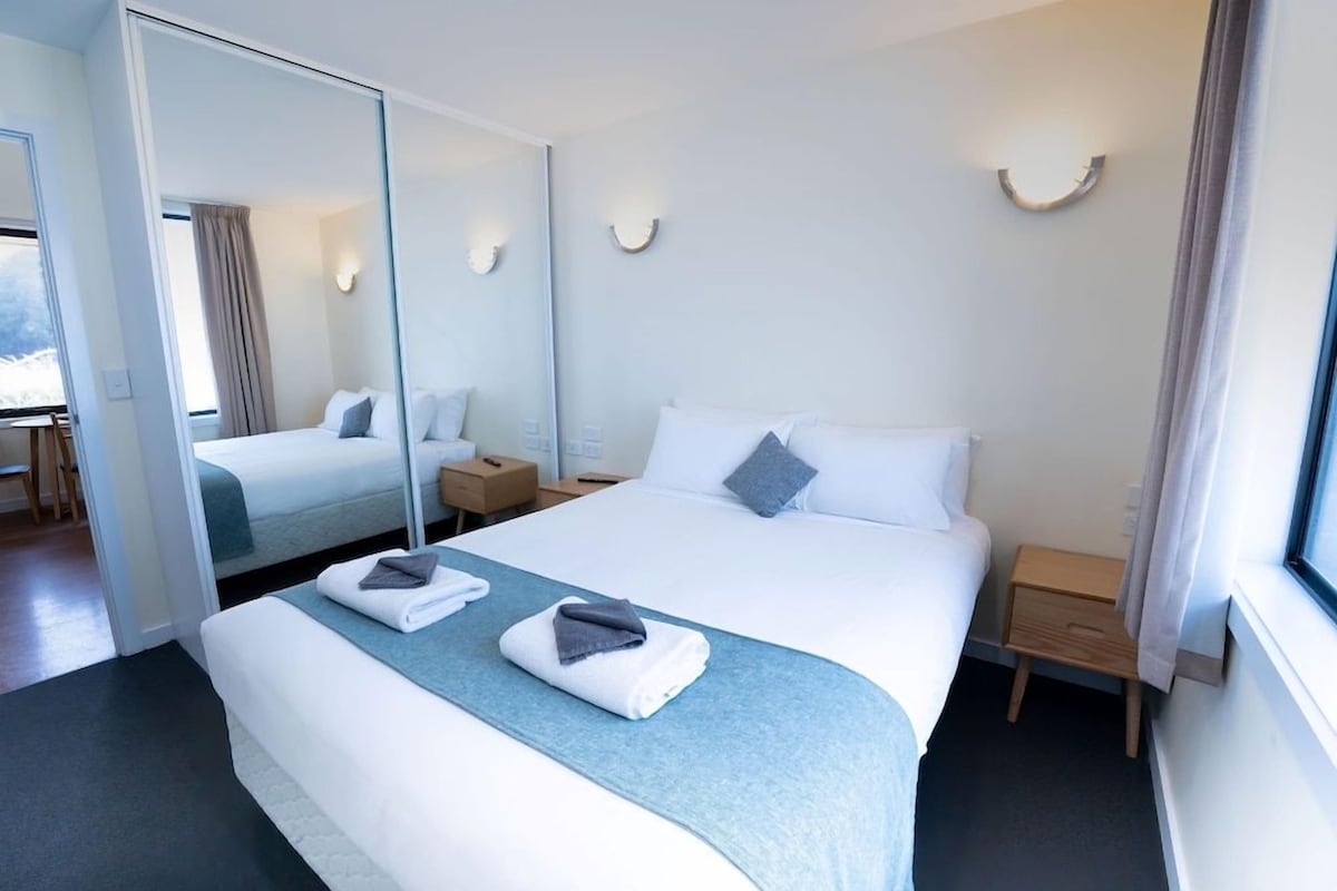 A hotel room with a large bed, a bedside table, a mirror, and a window.