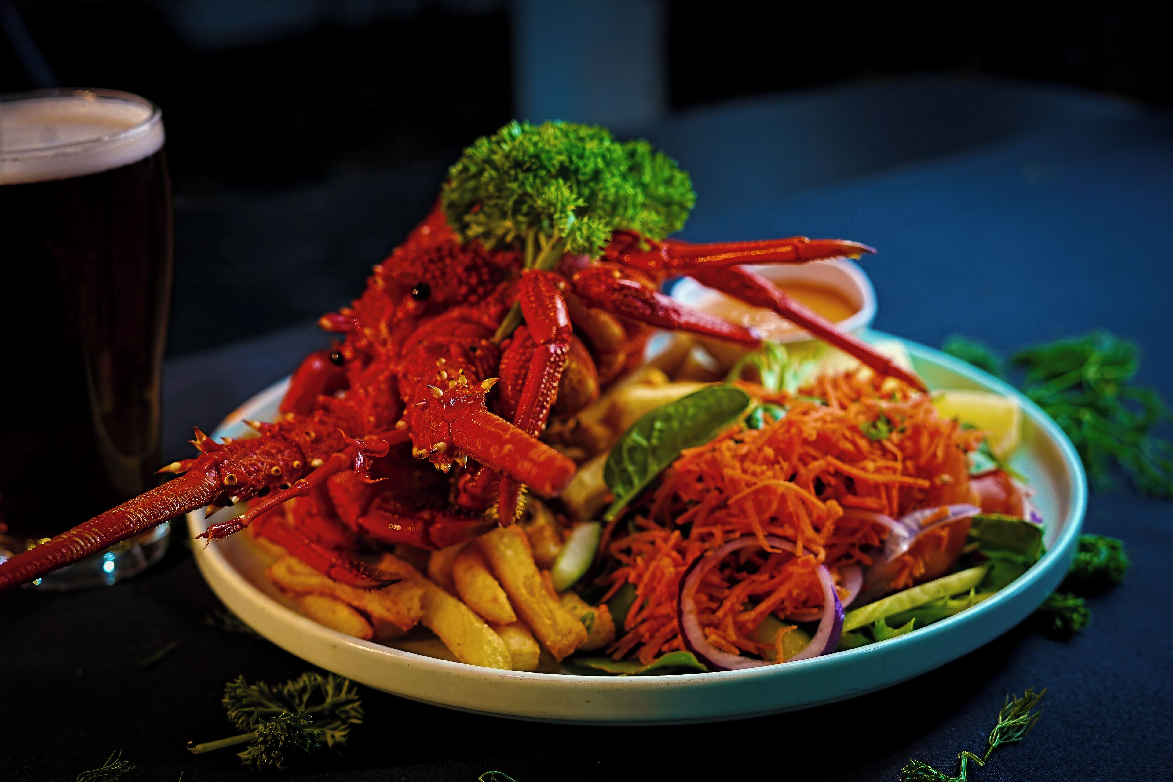 A plate of food with a lobster, fries, and salad, accompanied by a glass of beer.
