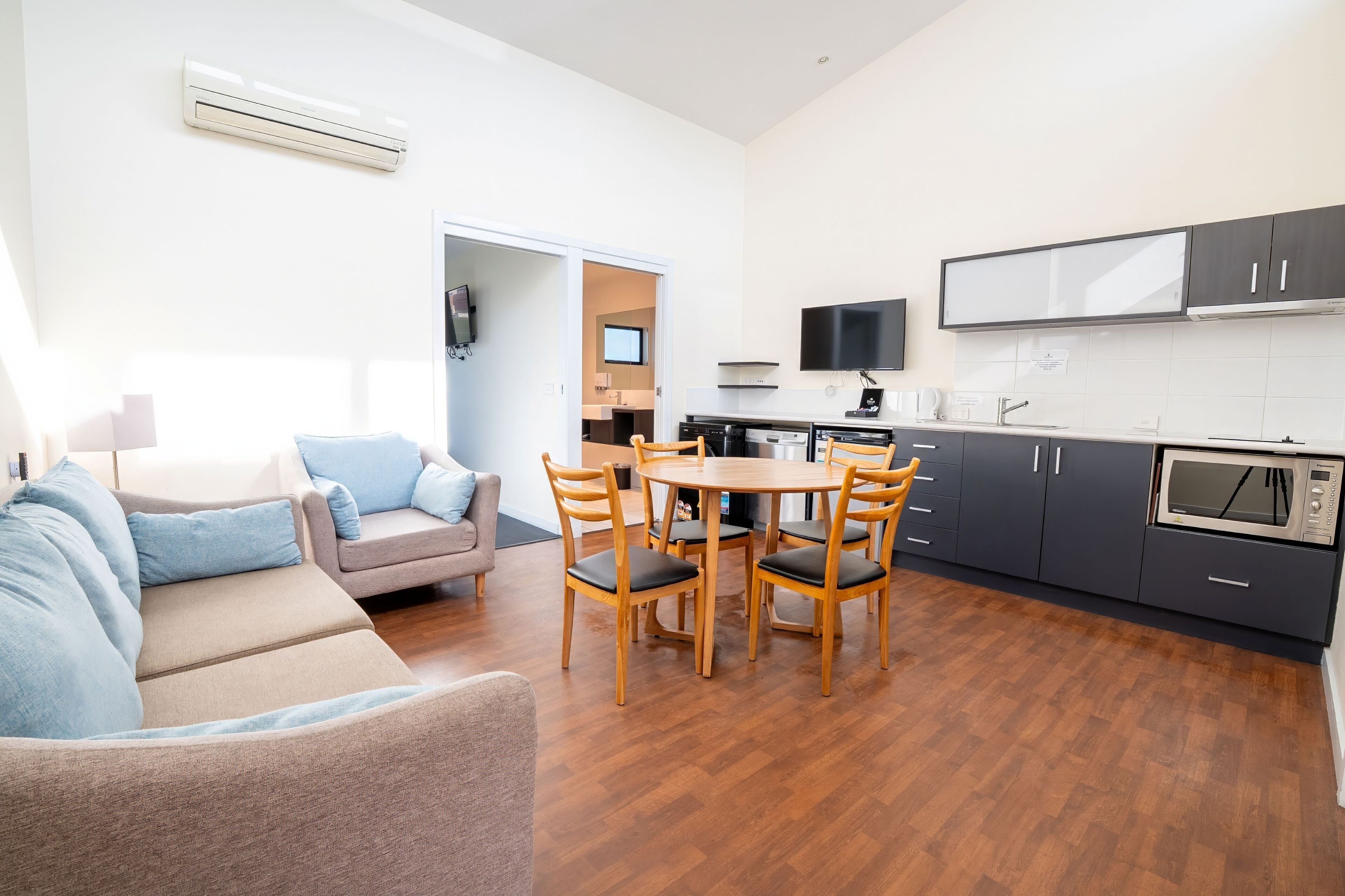 Een moderne woonkamer met een bank, een eettafel met stoelen, en een keuken met kasten en apparatuur.