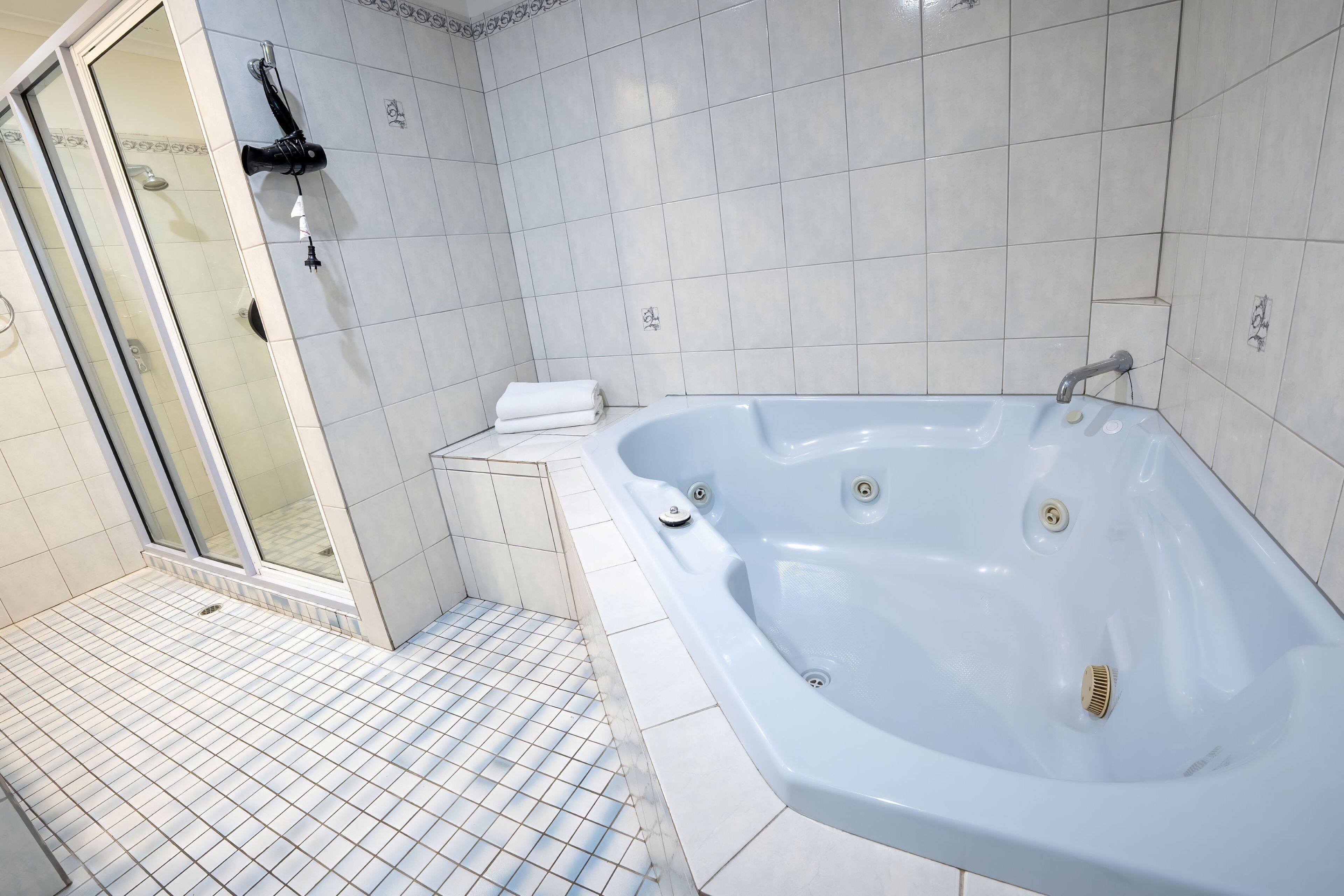 Une salle de bain moderne avec une grande baignoire, une douche à l’italienne en verre et un carrelage au sol.