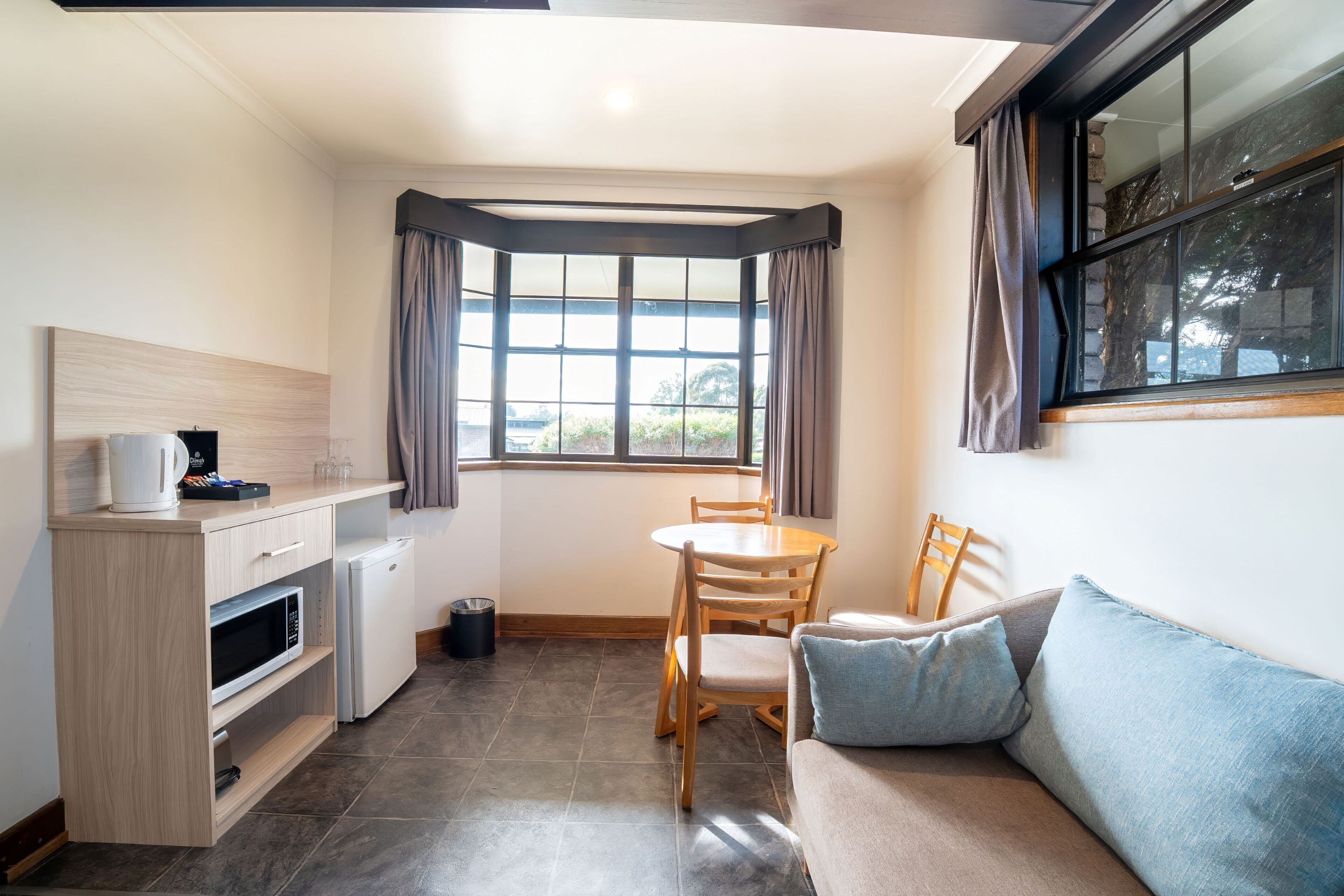 Una cocina compacta con comedor, microondas, refrigerador pequeño y ventana con cortinas.