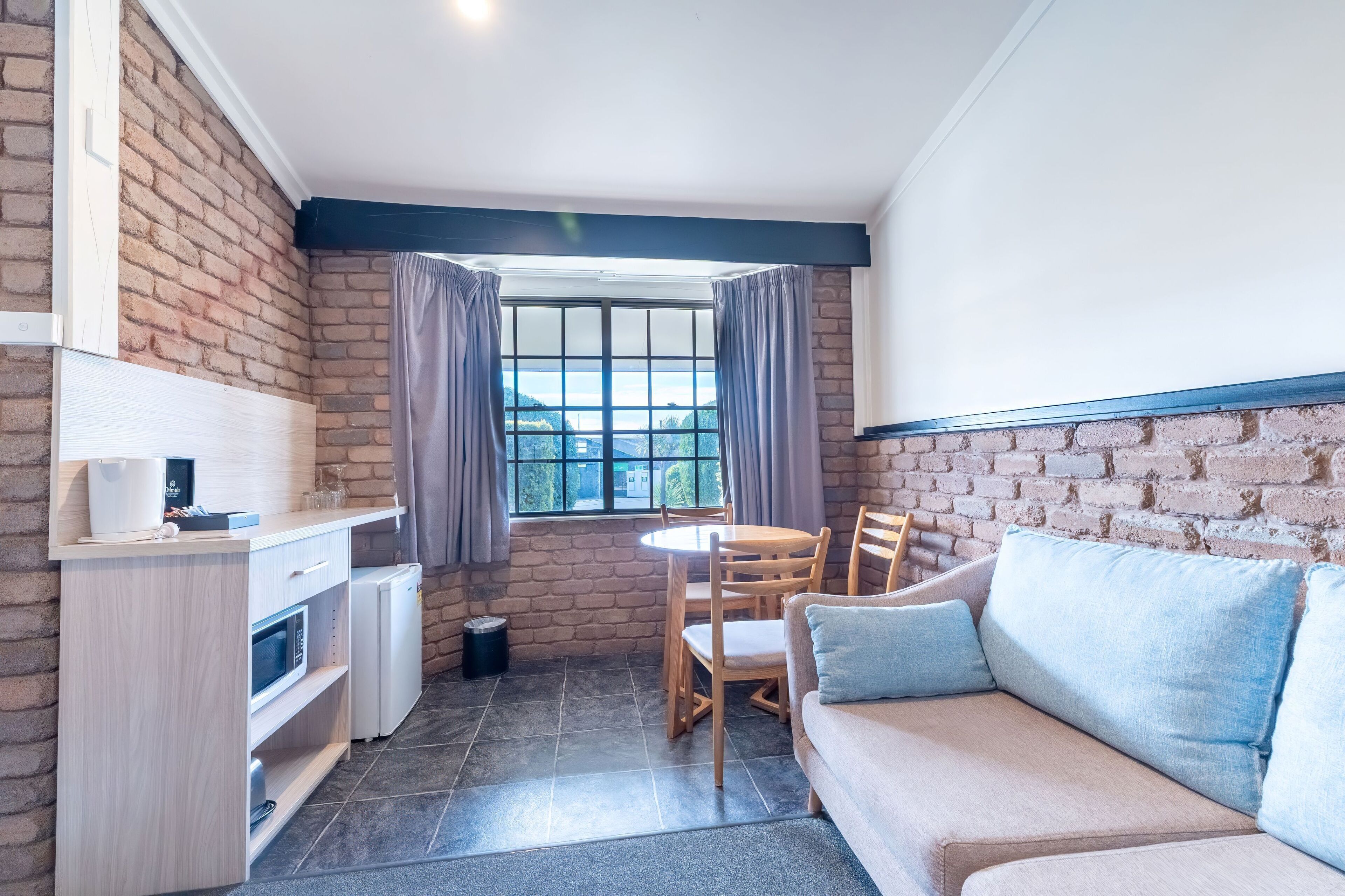 A compact kitchen with a dining area, a sofa, and a window with curtains.