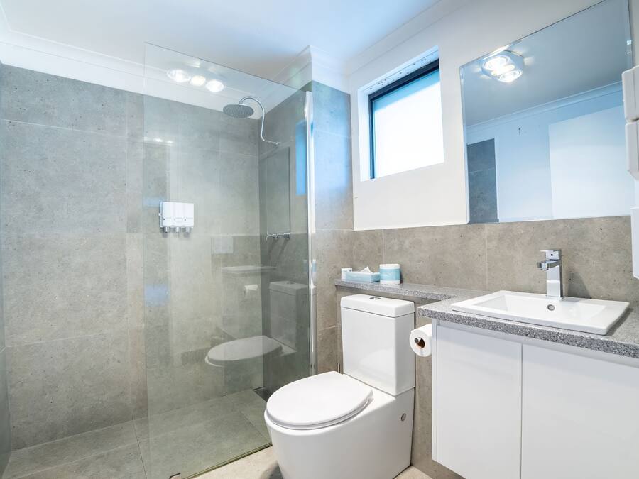 A modern bathroom with a glass-enclosed shower, a white toilet, and a sink with a mirror above it.