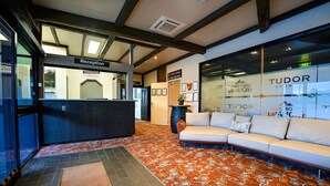 Un espace d’accueil comprenant un comptoir de réception, un canapé blanc, une moquette à motifs et un mur en verre orné du logo « TUDOR ».