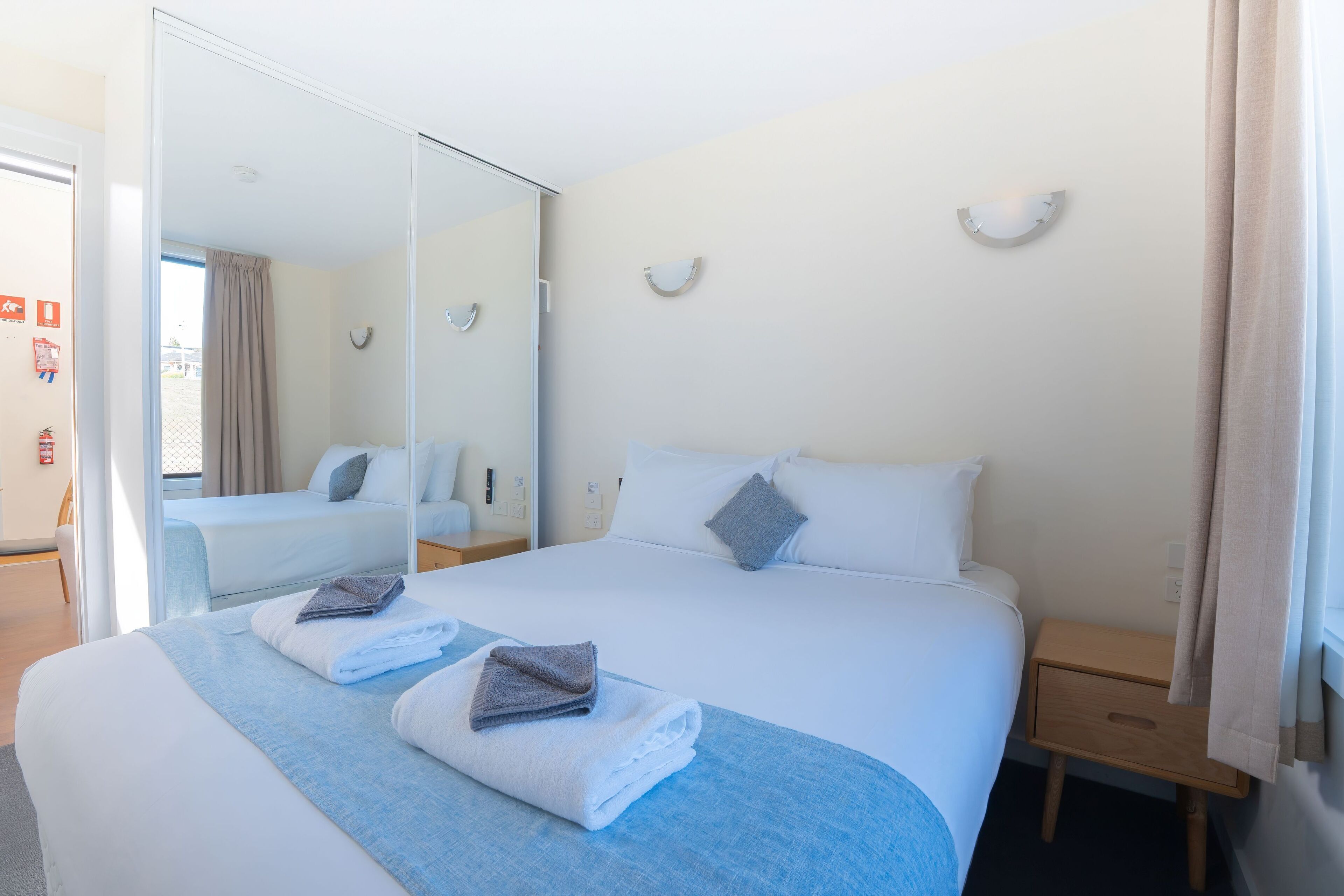 A hotel room with a large bed, a bedside table, a mirror, and a window with curtains.