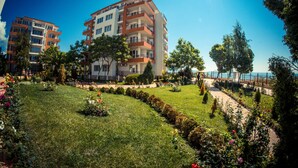 A multi-story residential building with balconies, surrounded by well-maintained gardens and a pathway. - Riviera Fort Beach (Ravda)