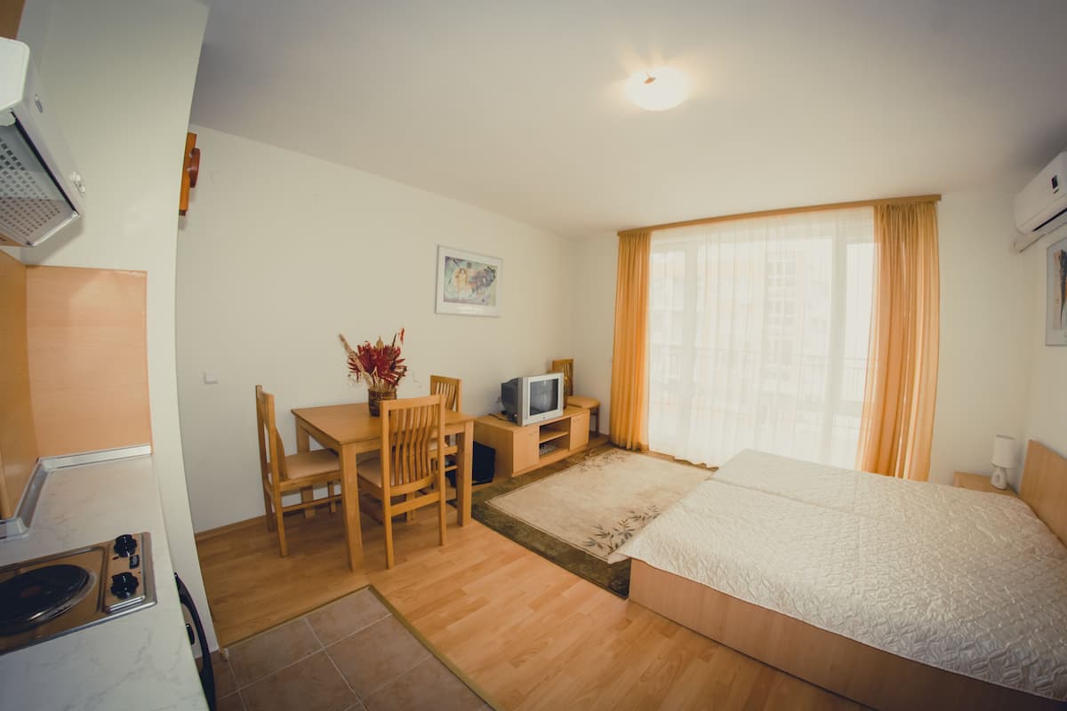 A compact hotel room with a bed, a desk with a chair, a television, and a small table with a vase of flowers.