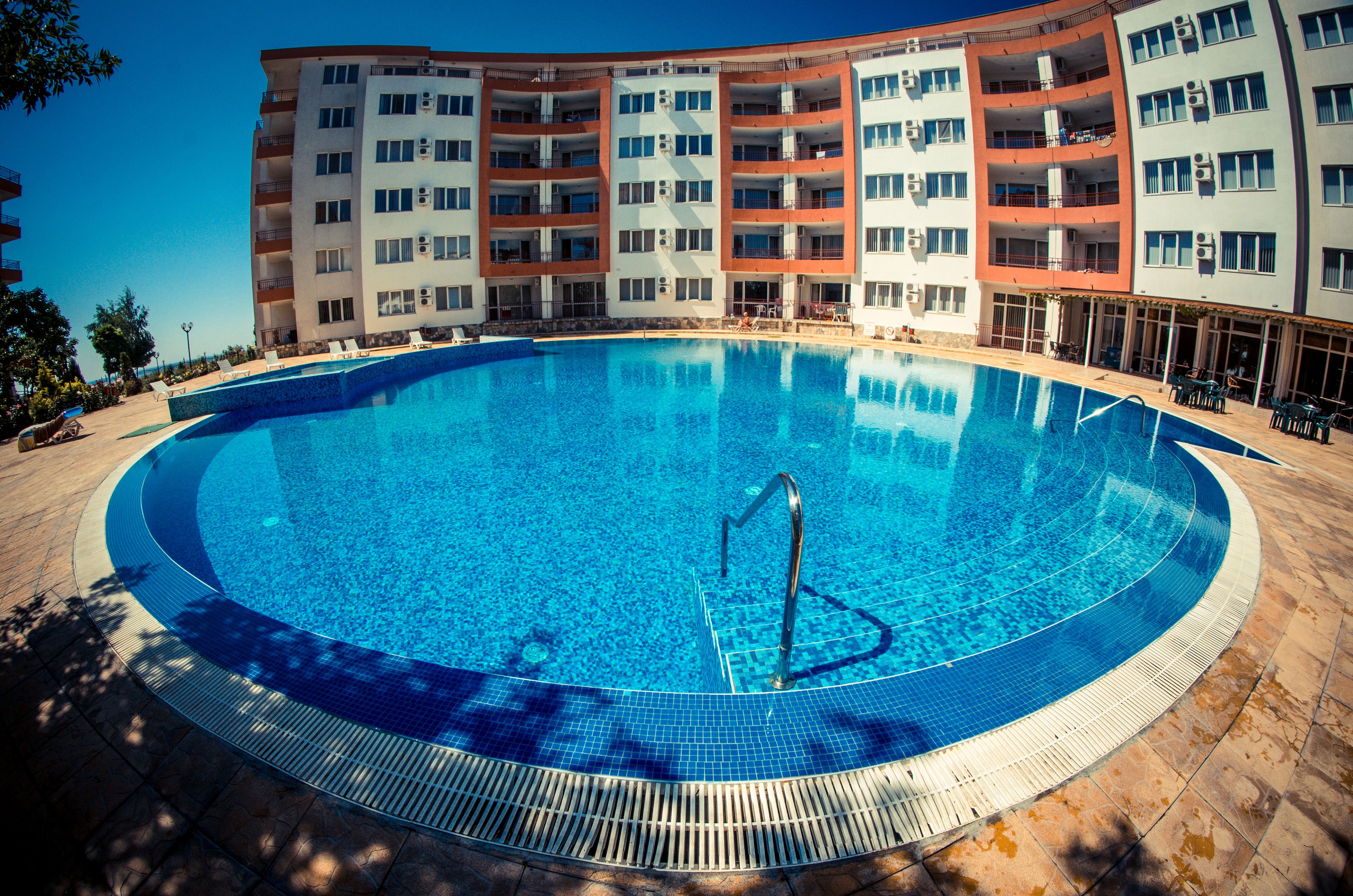 A large, clear swimming pool with a pool ladder, surrounded by a tiled deck.