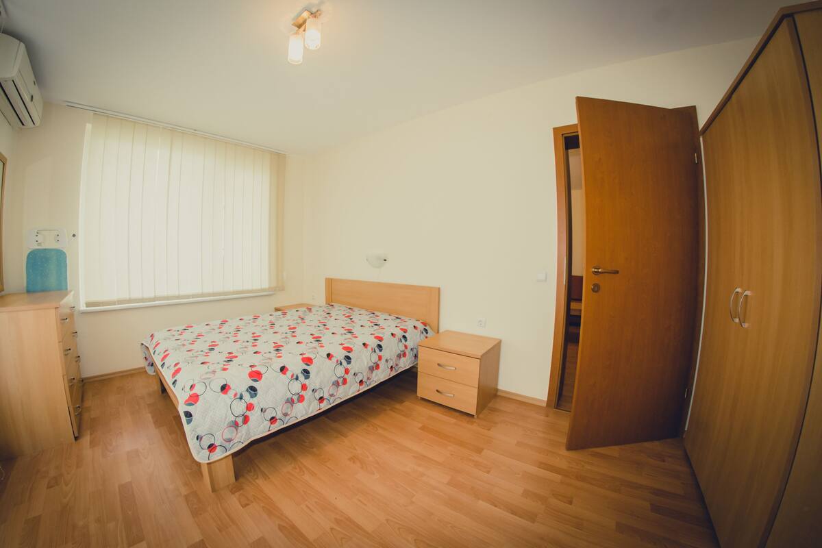 Un dormitorio con cama, un armario de madera, una mesita de noche y una ventana con persianas.