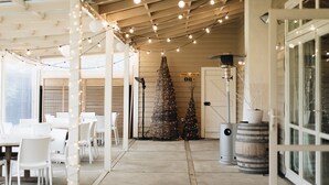 A covered outdoor seating area with string lights, white chairs, and two Christmas trees.