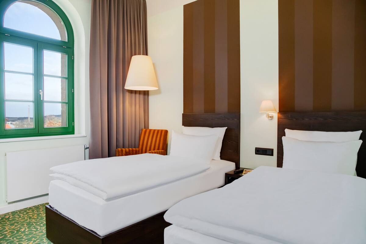Habitación de hotel con dos camas, una ventana con cortinas, una lámpara y vistas al exterior.