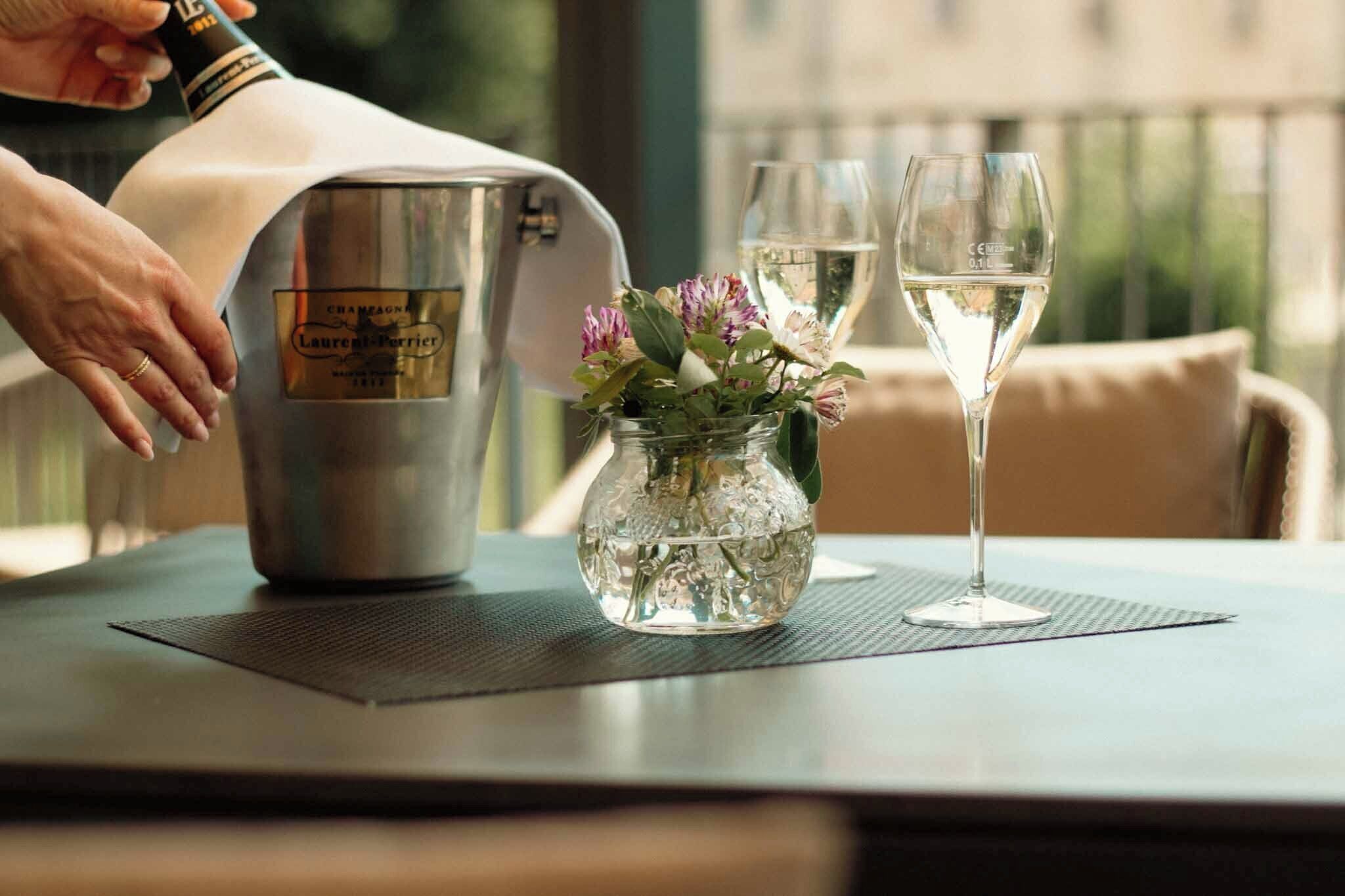 A table with a champagne bucket, a glass of white wine, and a vase with flowers.