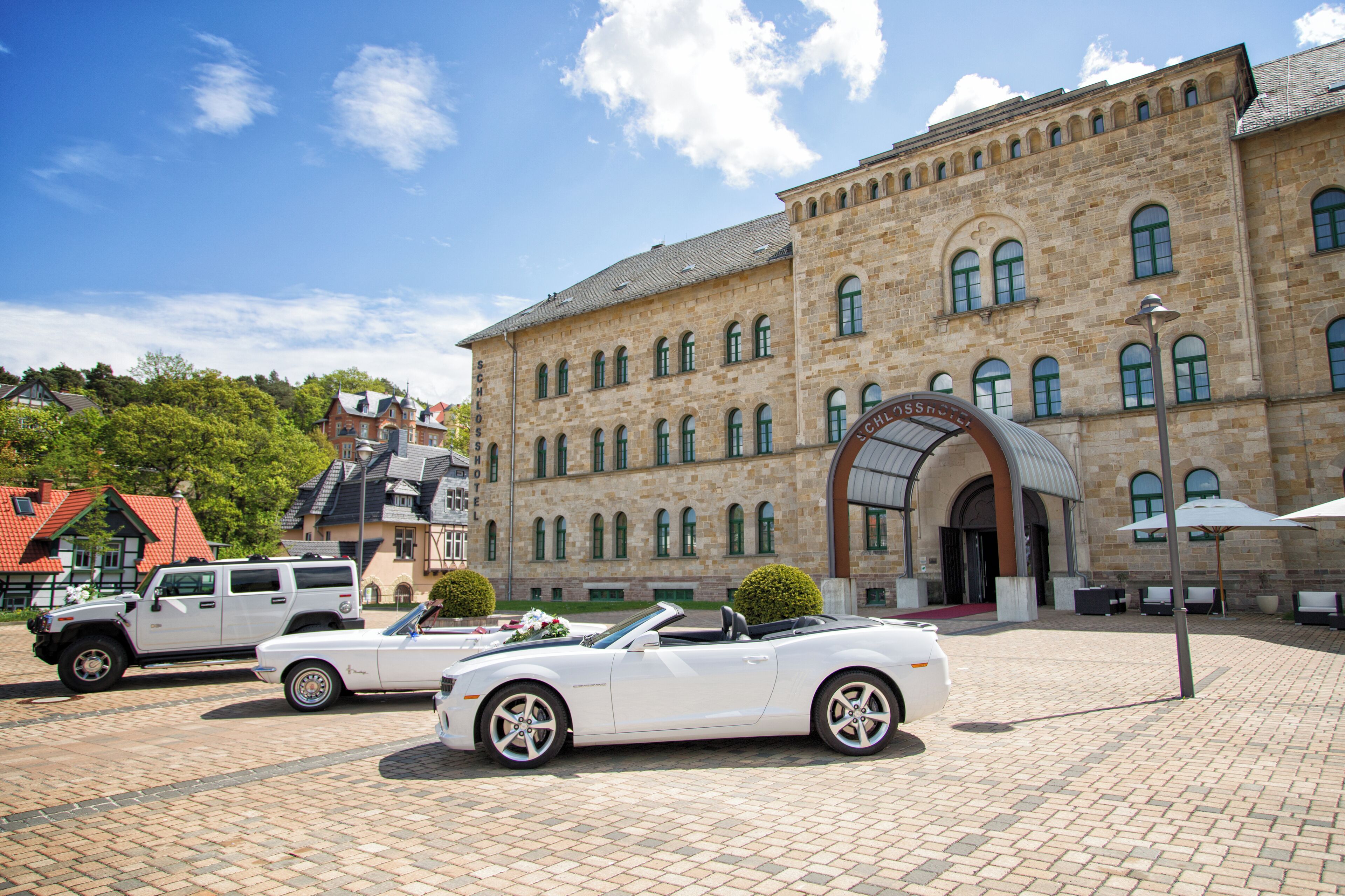 A historic building with a courtyard, a white convertible, and a white SUV parked in front.