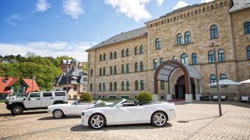 Ein historisches Gebäude mit Innenhof, einem weißen Cabrio und einem weißen SUV davor.