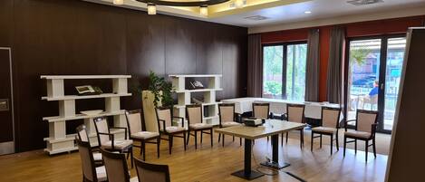 A hotel room with a wooden floor, a large window with curtains, a chandelier, and white shelving units.