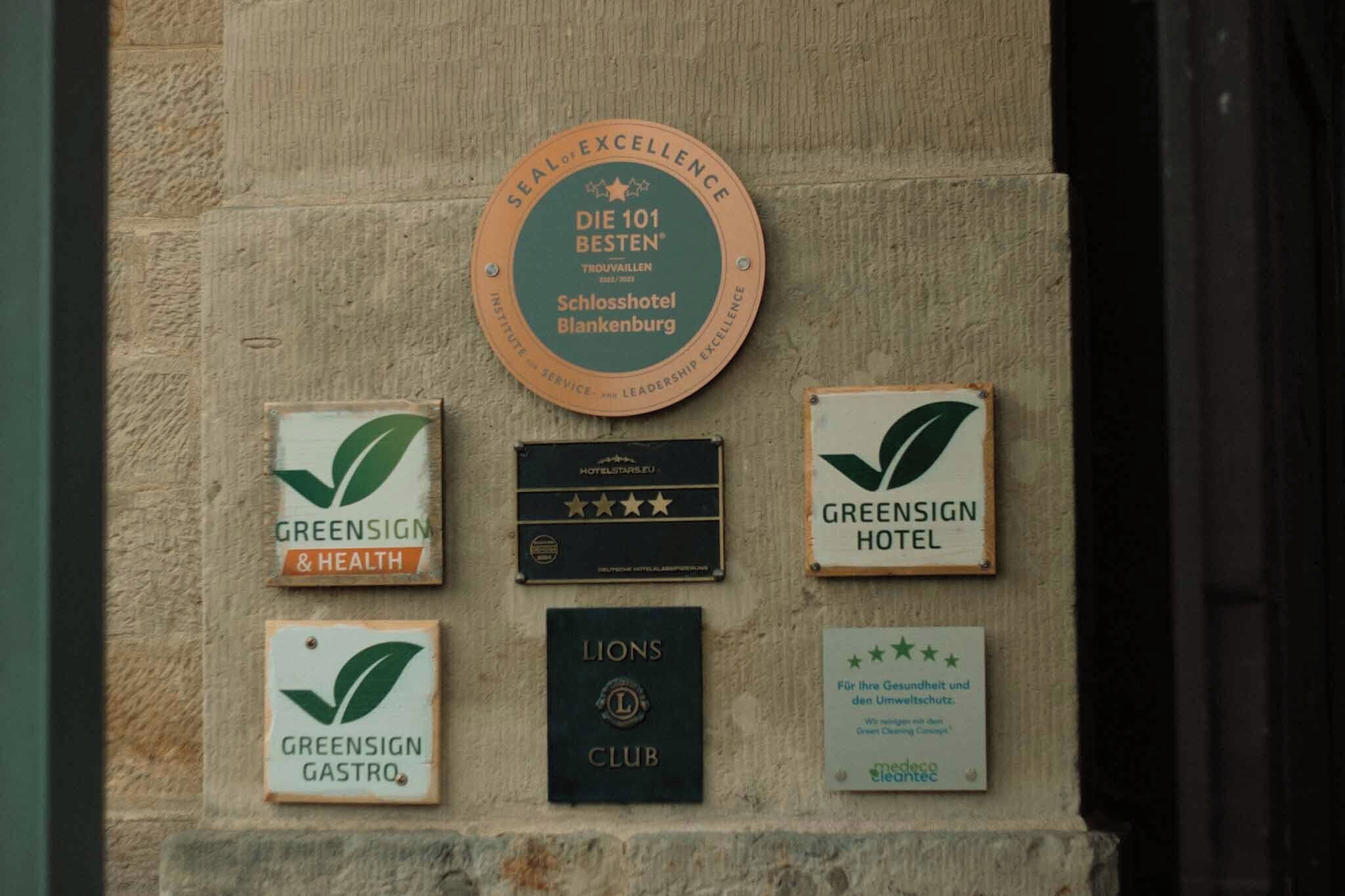 A wall with multiple plaques, including one for 'Die 101 Besten' and others for 'Greensign Hotel', 'Greensign & Health', 'Greensign Gastro', and 'Lions Club'.