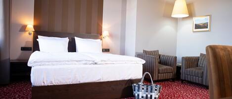 Habitación de hotel con una cama grande, dos sillones, una mesita pequeña y una alfombra roja estampada.