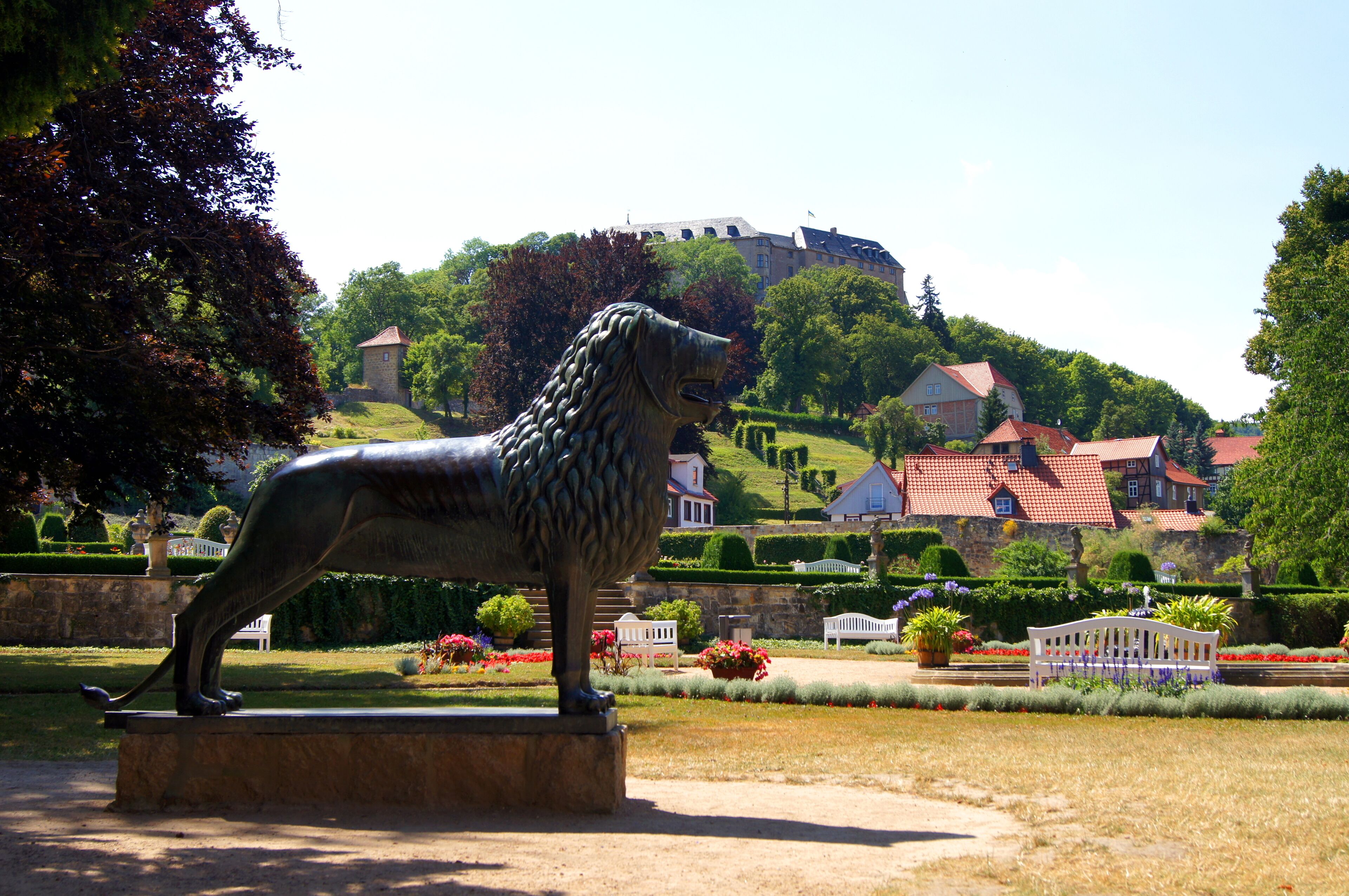 A bronze lion statue in a park with a castle in the background.
