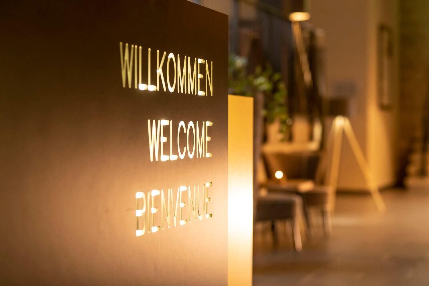 Une enseigne avec les mots « WILLKOMMEN », « WELCOME » et « BIENVENUE » écrits en lettres lumineuses.