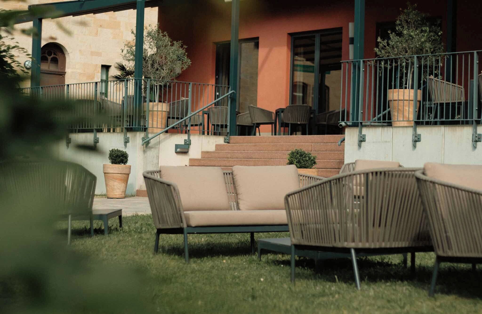 An outdoor seating area with wicker chairs and a small table, a staircase leading to a building, and potted plants.