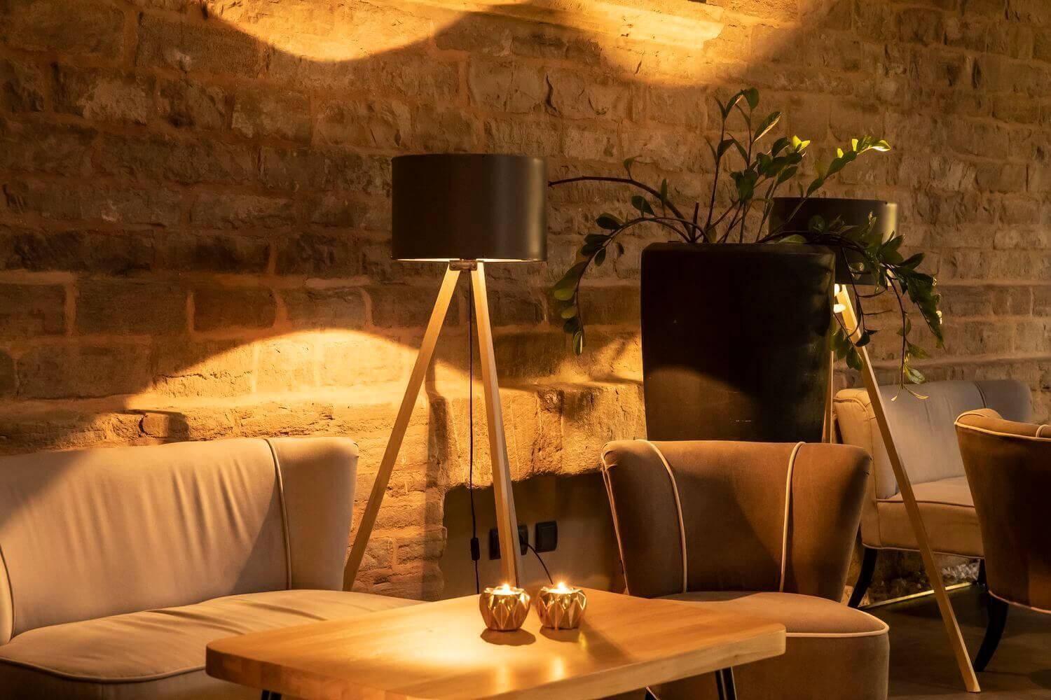 Um quarto aconchegante com parede de pedra, luminária de chão moderna, planta em vaso e mesa de madeira com velas.