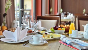 A breakfast setting with a table set for two, including plates, glasses, a bowl of fruit, croissants, and a newspaper. - Schlosshotel Blankenburg (Blankenburg)