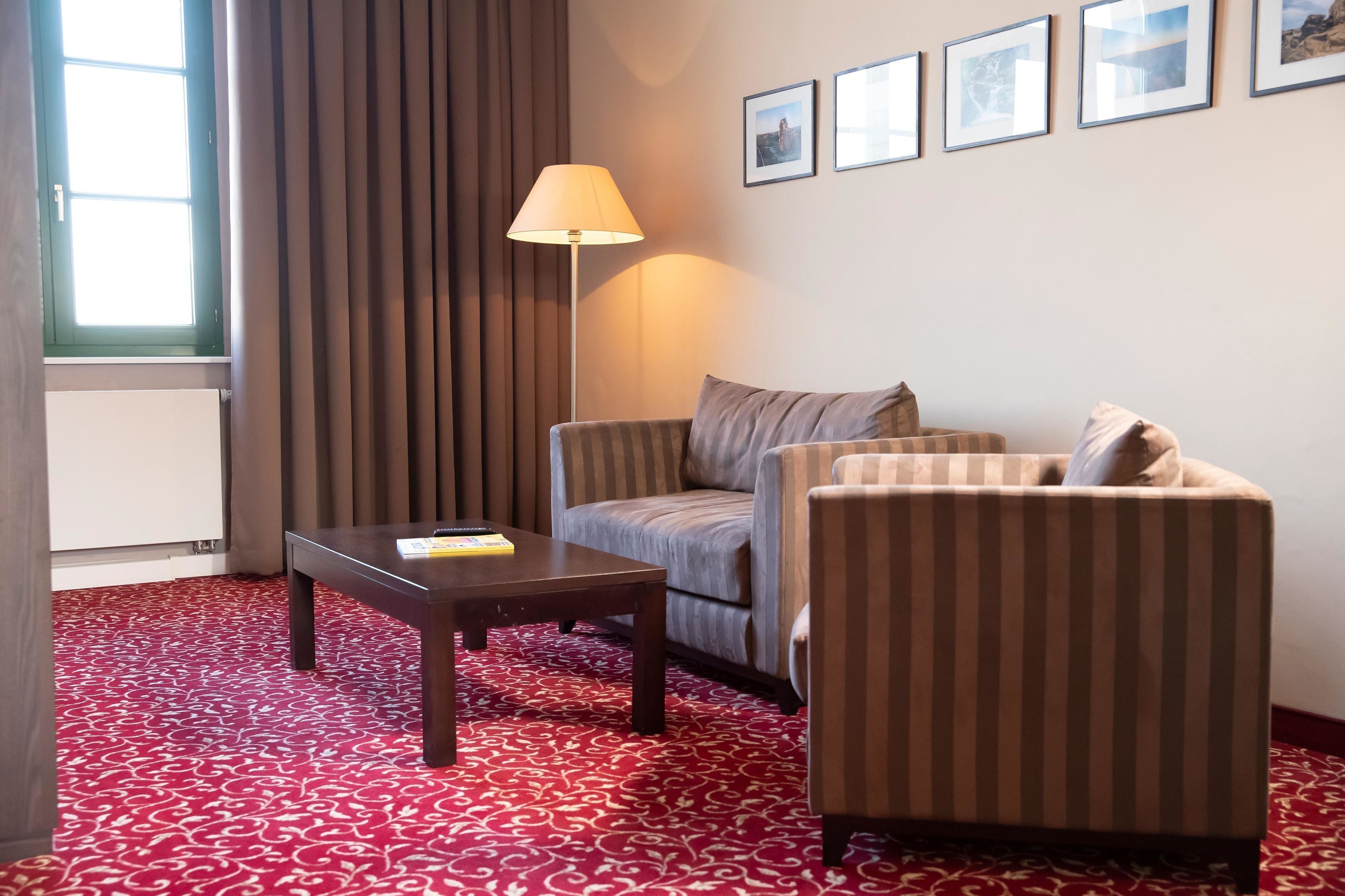 Une chambre d’hôtel avec un canapé à rayures, une petite table avec une lampe et un tapis rouge à motifs.
