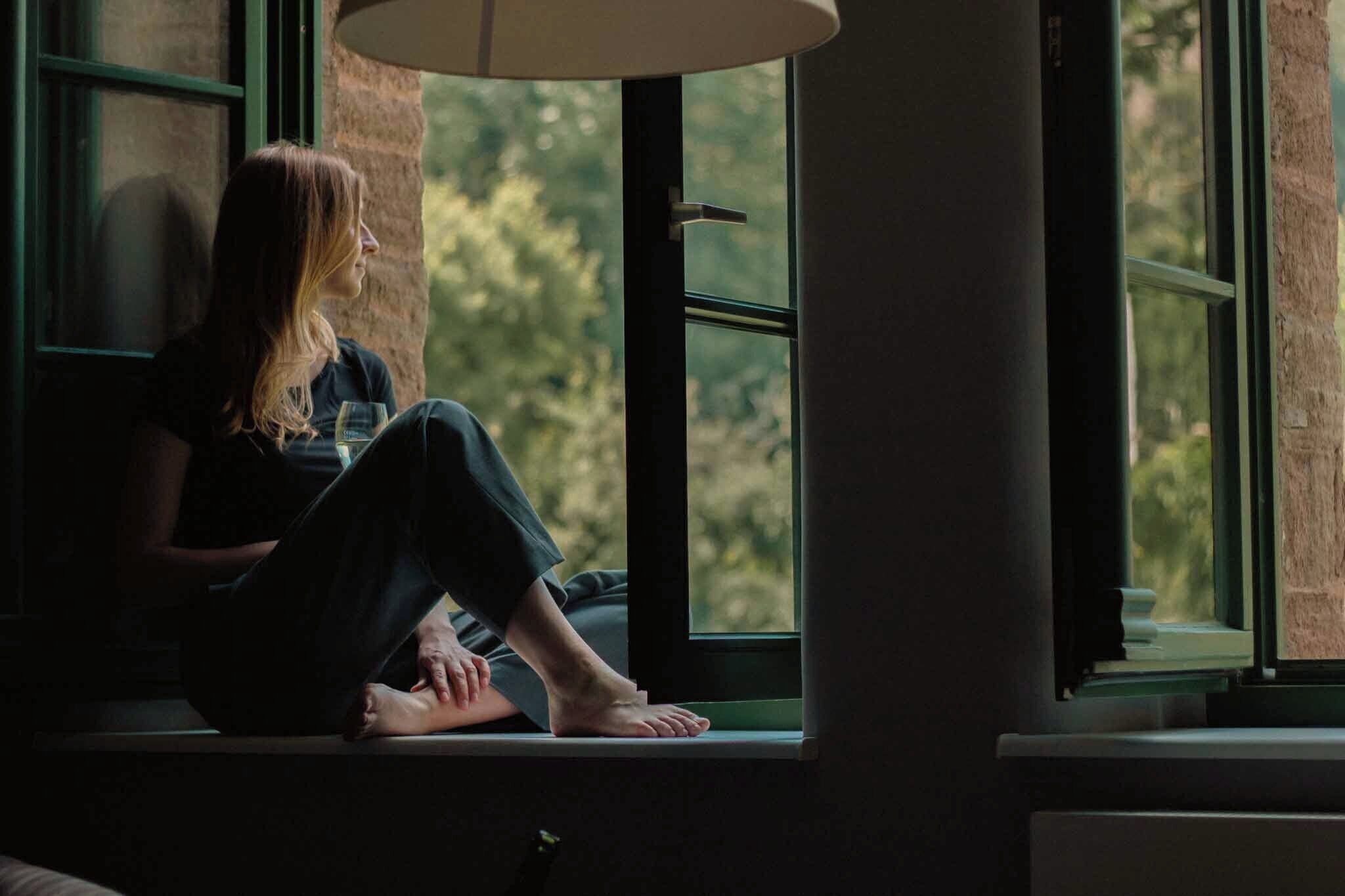 A person sitting by a window with a view of greenery outside.