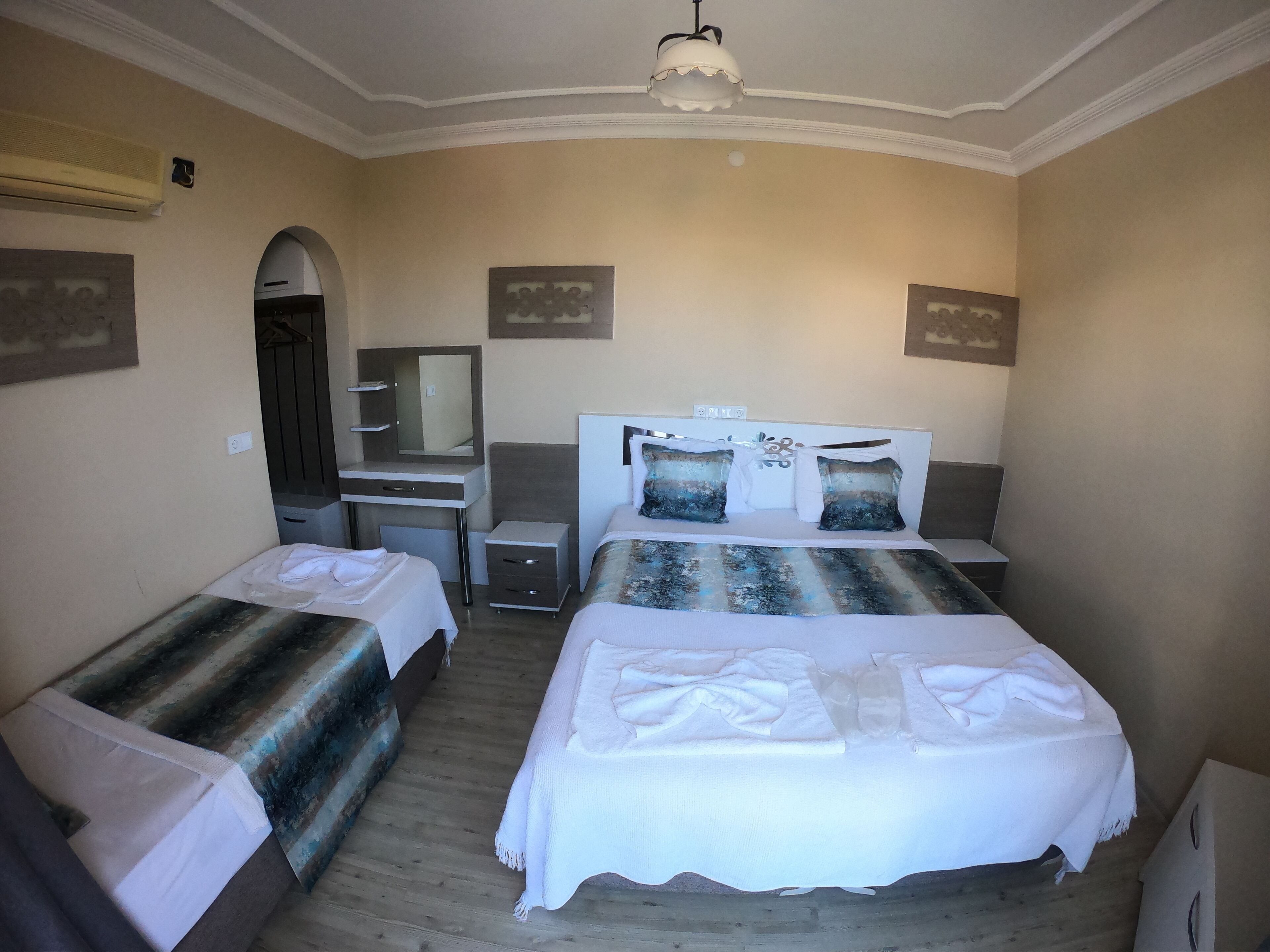 A hotel room with two single beds, a desk with a chair, a vanity with a mirror, and a ceiling light fixture.