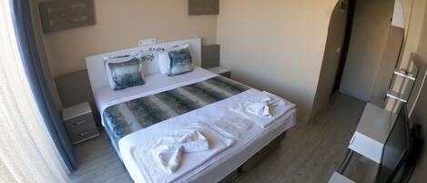 Habitación de hotel con cama, mesitas de noche, aire acondicionado, un espejo y una puerta que da a otra habitación.