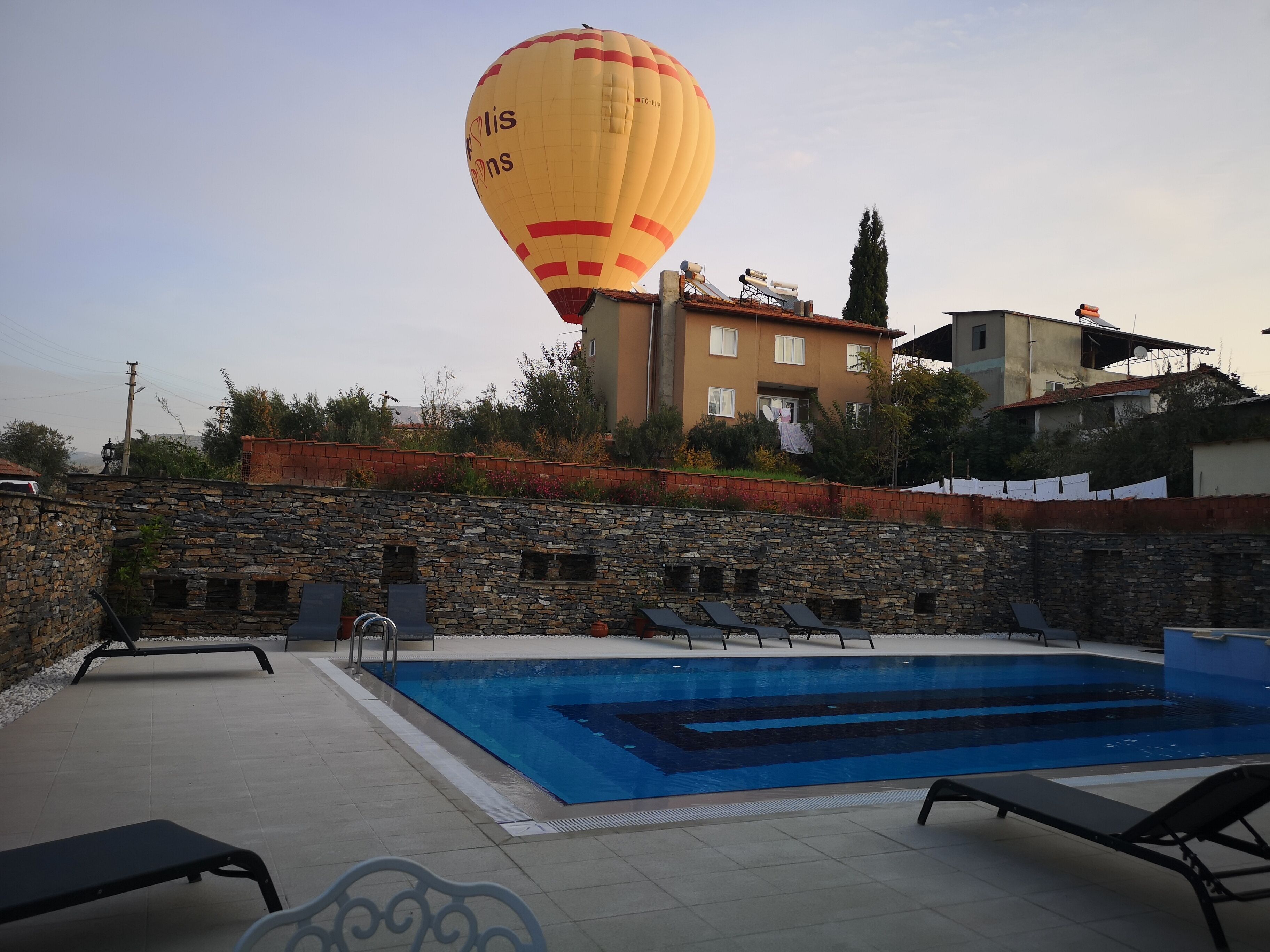 Una piscina con sillas de descanso y un globo aerostático al fondo.