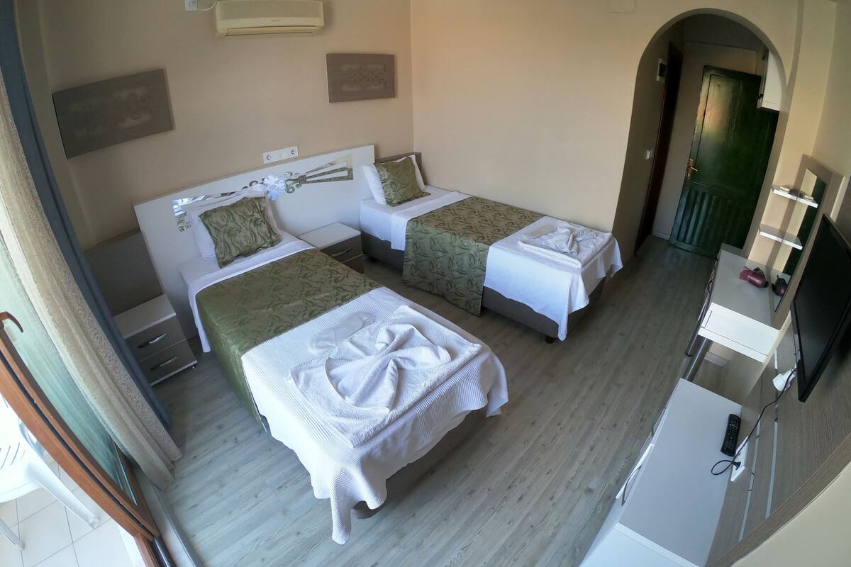 A hotel room with two beds, a desk, a TV, and a door leading to another room.