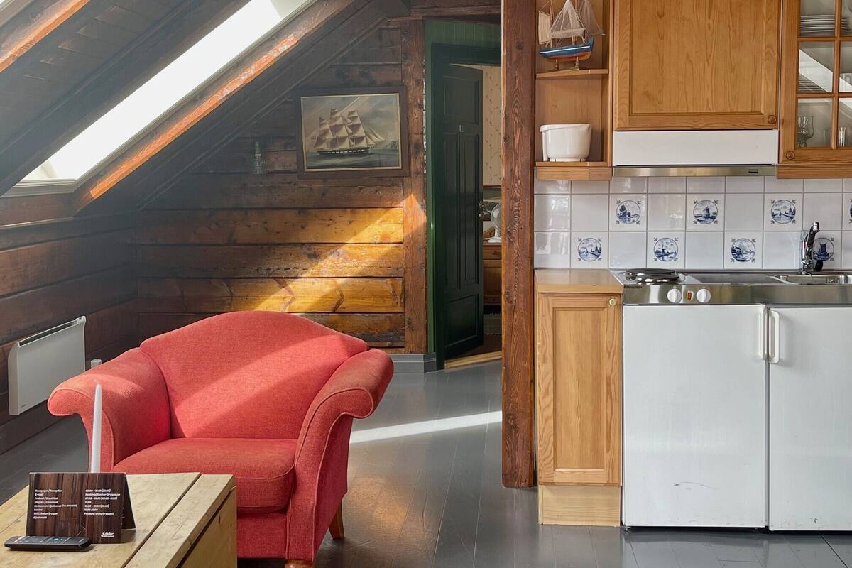 A cozy cabin interior with a red armchair, wooden cabinets, a tiled backsplash, and a skylight.
