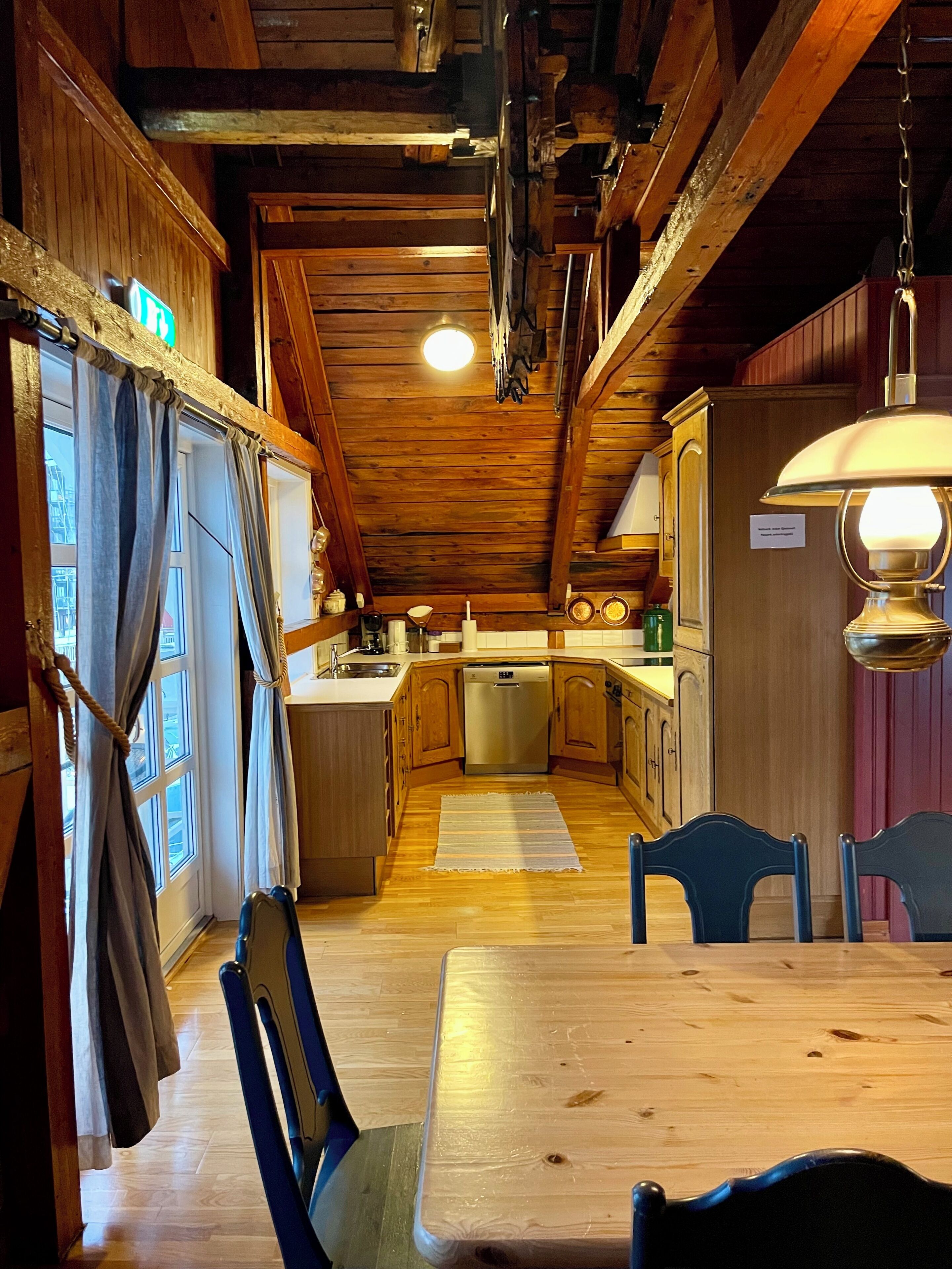 Interior rústic de fusta amb zona de menjador, cuina i vista per una finestra.