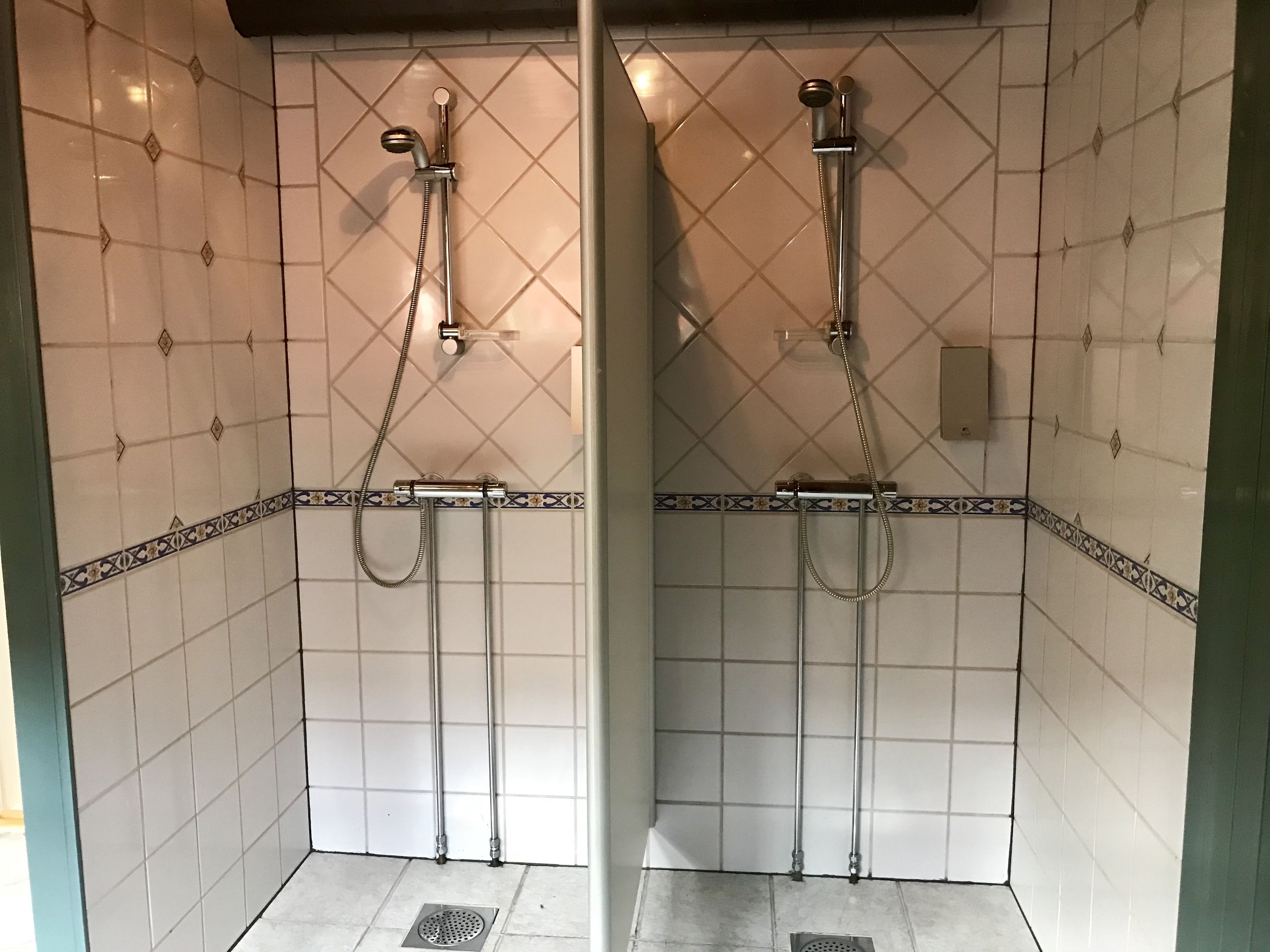 Une salle de bain avec deux cabines de douche, des murs carrelés et un drain au sol.